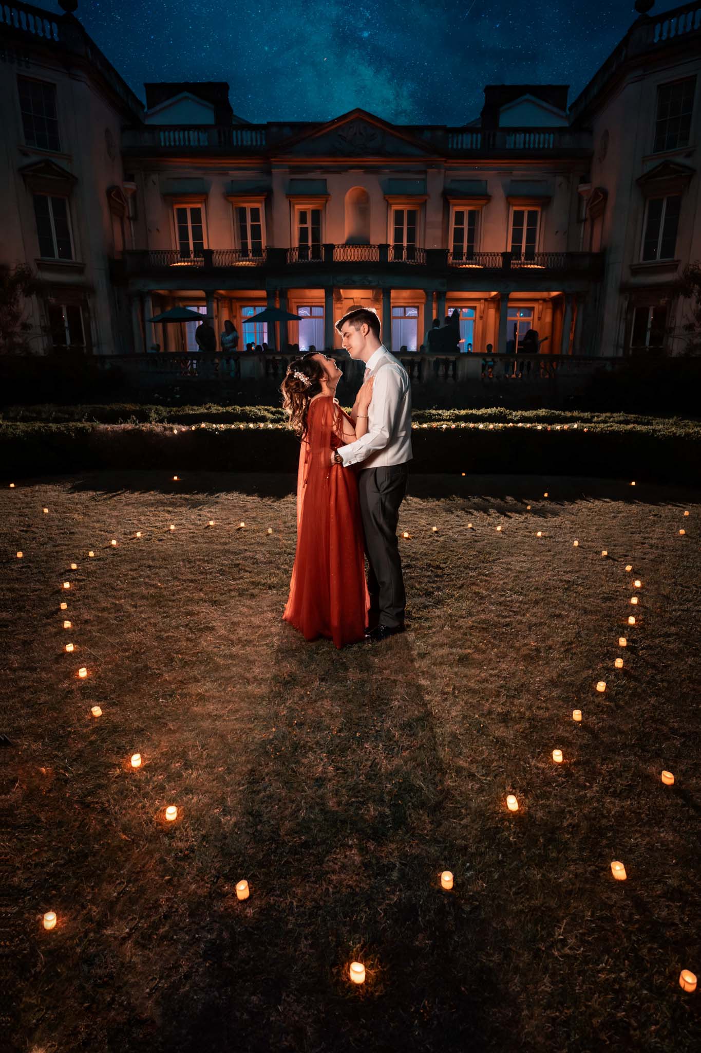 Fairytale wedding couple posing in front of a candlelit mansion. (listing)