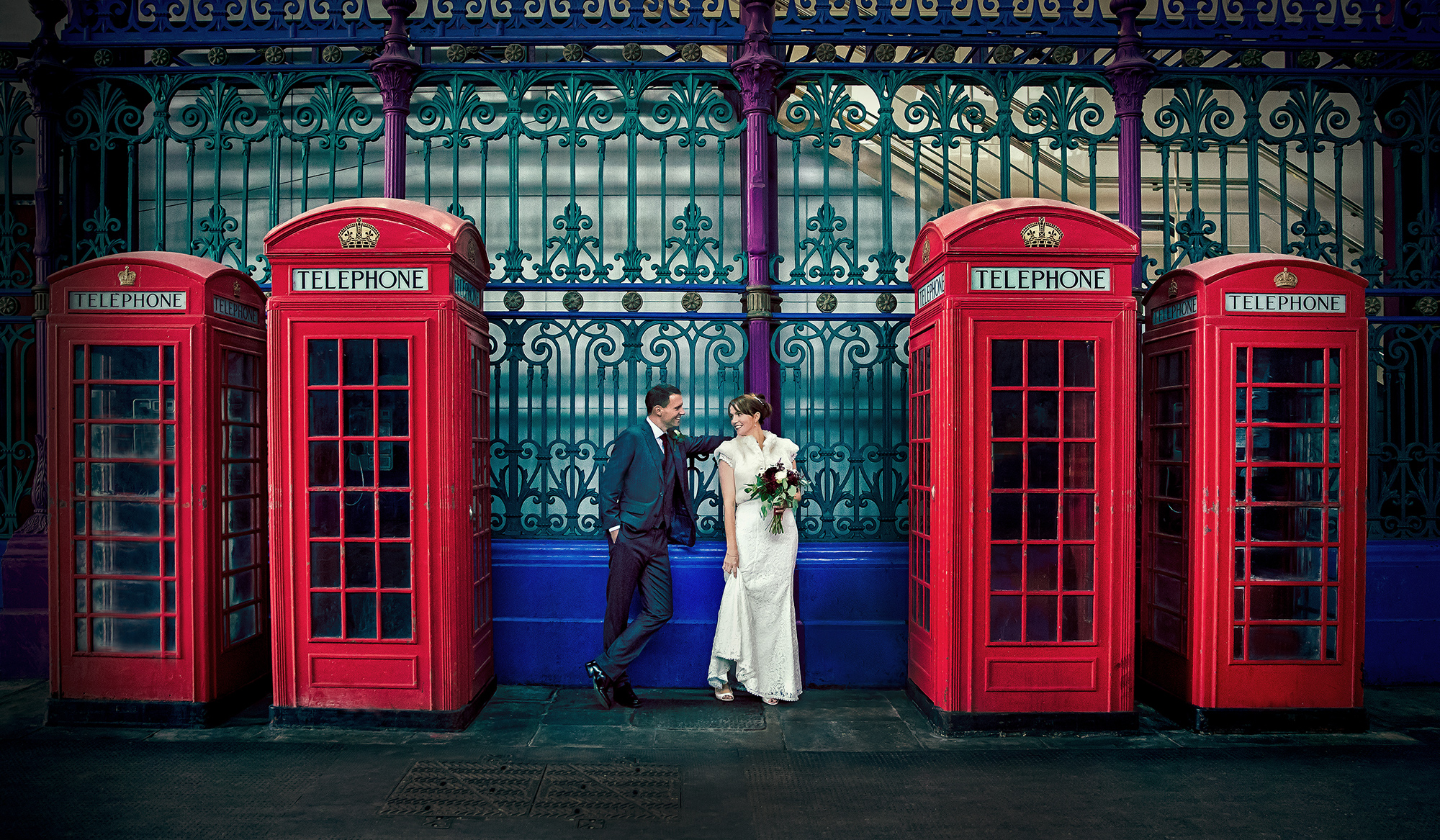 A wedding photographer duo capturing a bride and groom in front of telephone booths. (listing)