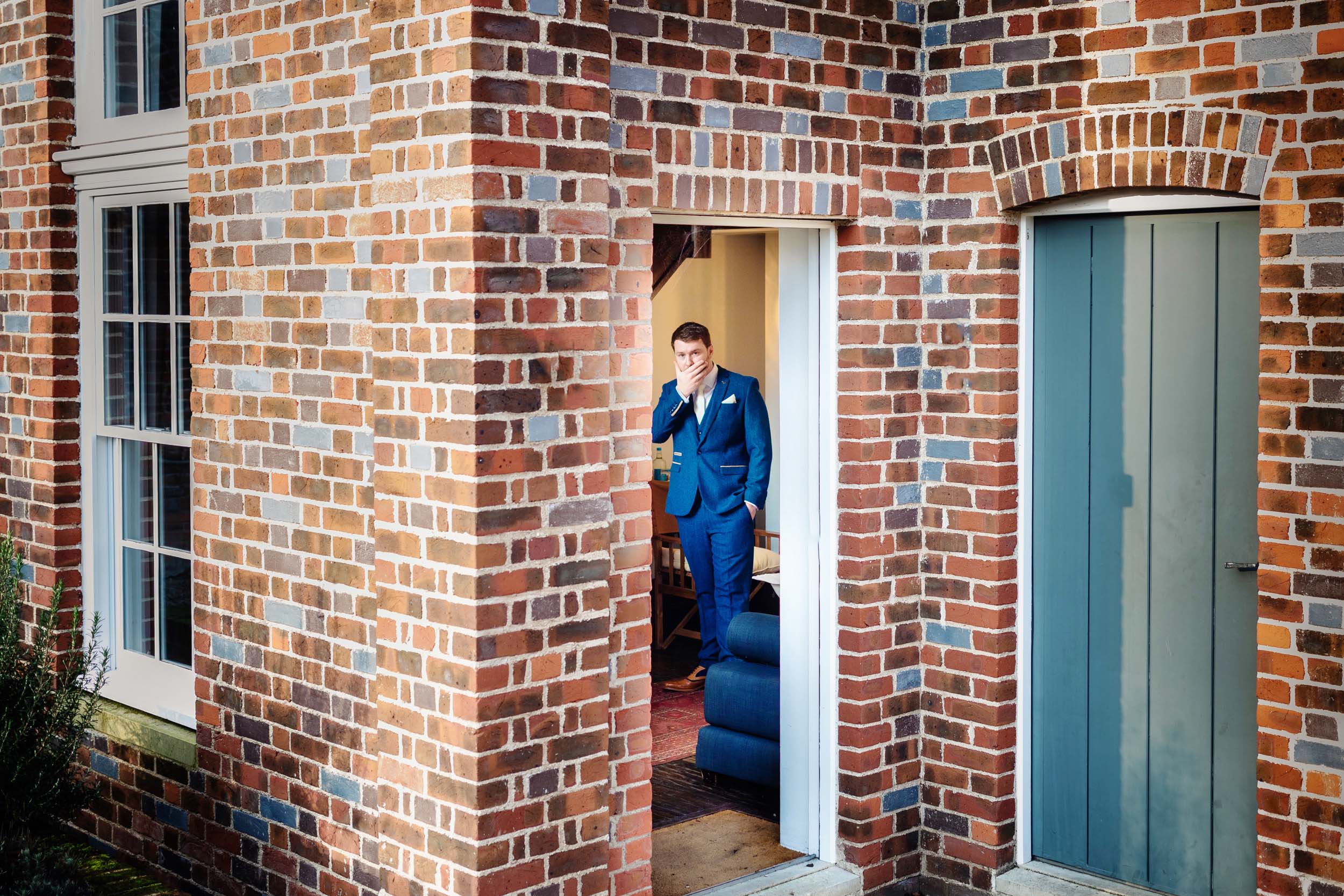 A man in a suit standing in the doorway of a brick house, cheap wedding. (listing)