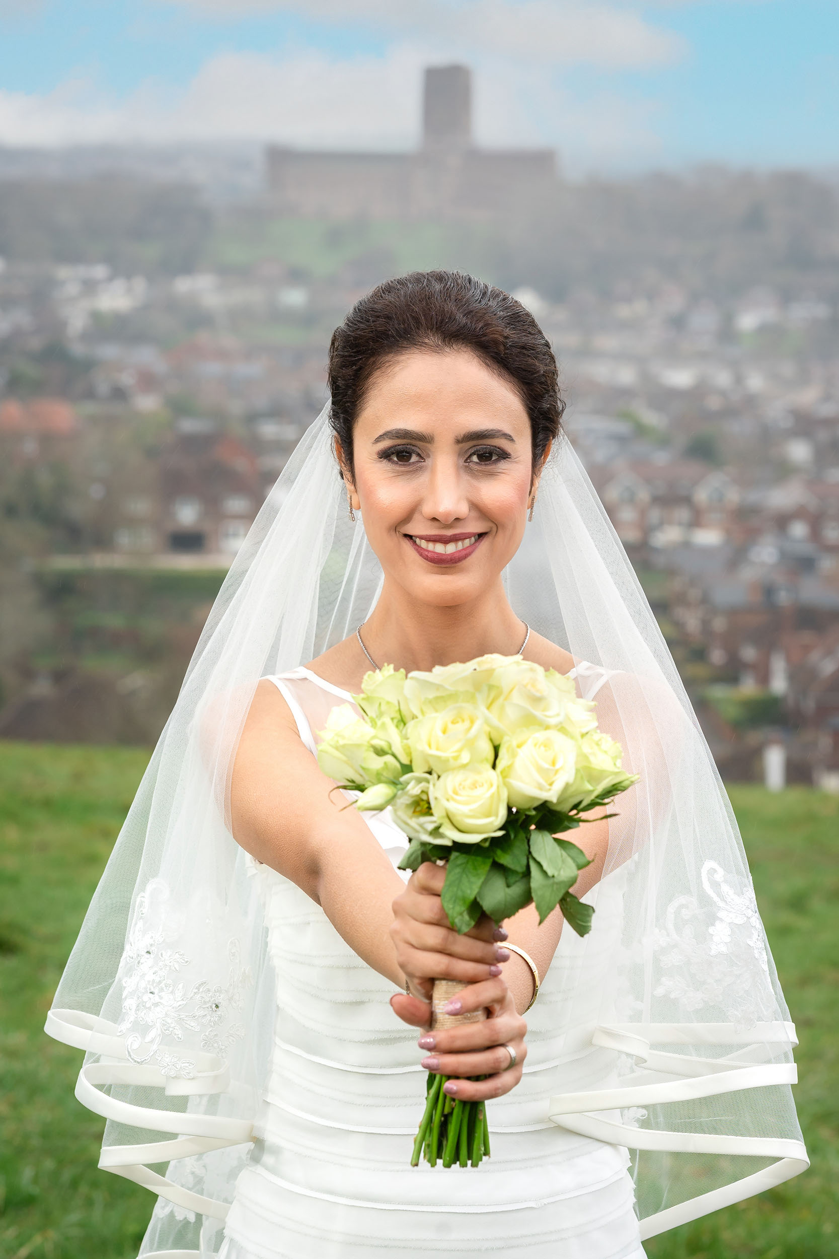 A bride holding a bouquet in front of a castle, captured by a cheap wedding photographer in London. (listing)