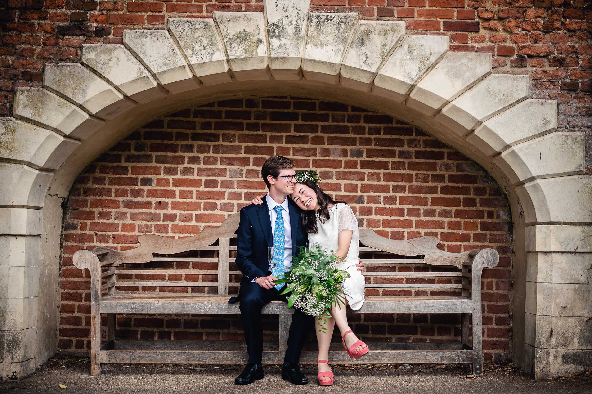 Cheap wedding photographer London captures a bride and groom sitting on a bench in a brick archway. (listing)
