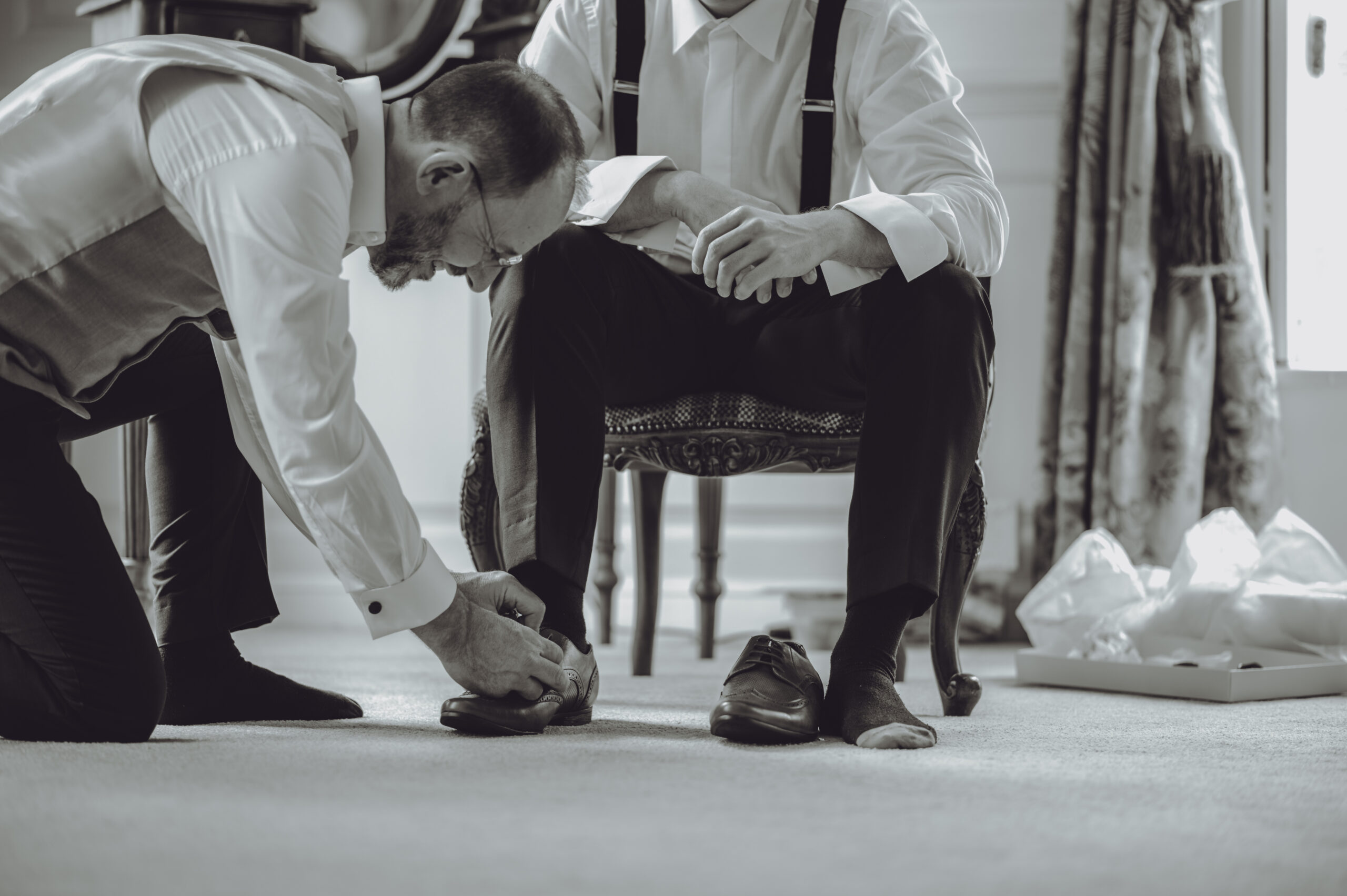 Two men putting on their shoes in a room. (listing)