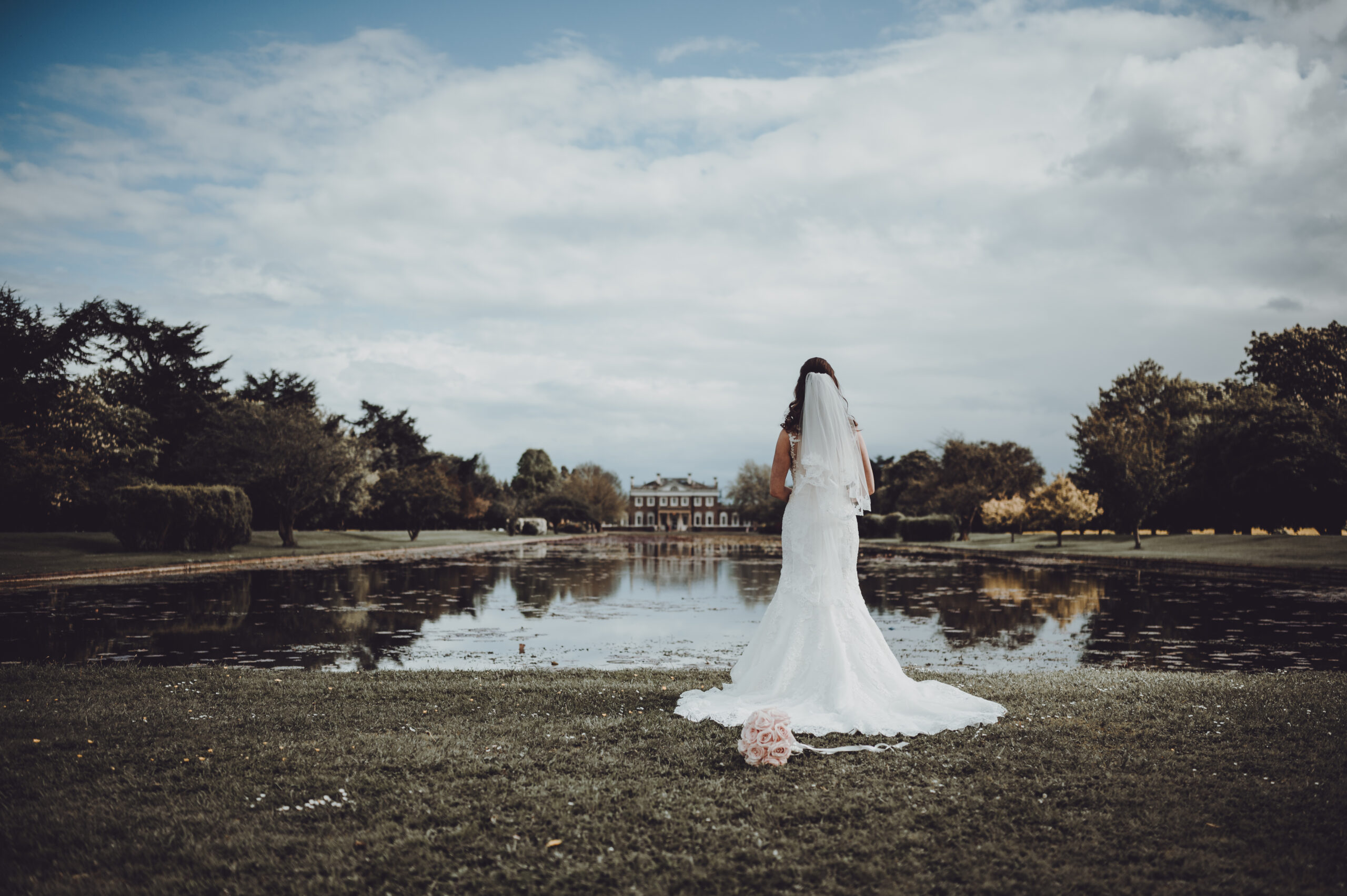 A bride standing in front of a pond. (listing)