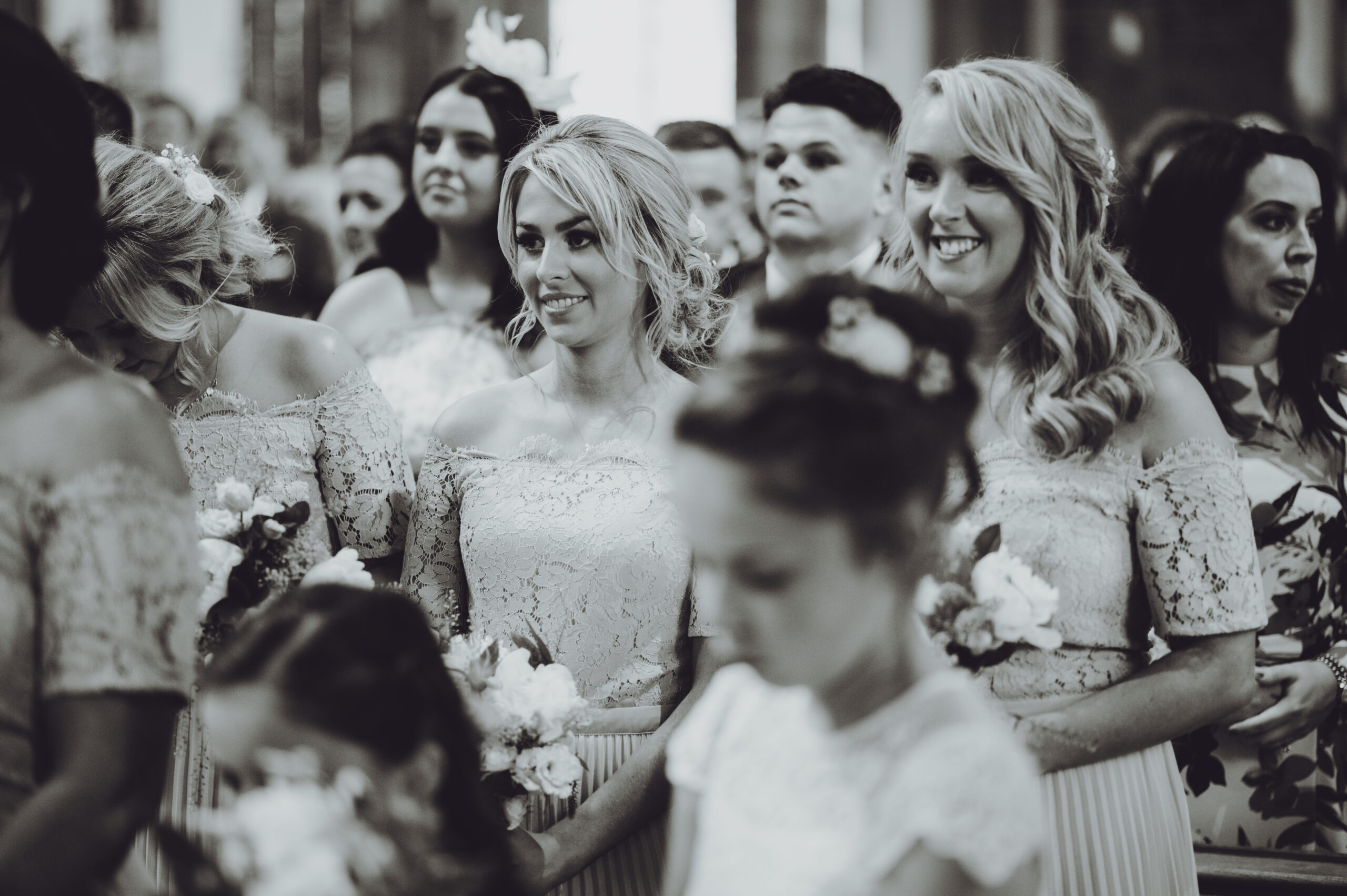 Bridesmaids smiling at each other in a church. (listing)