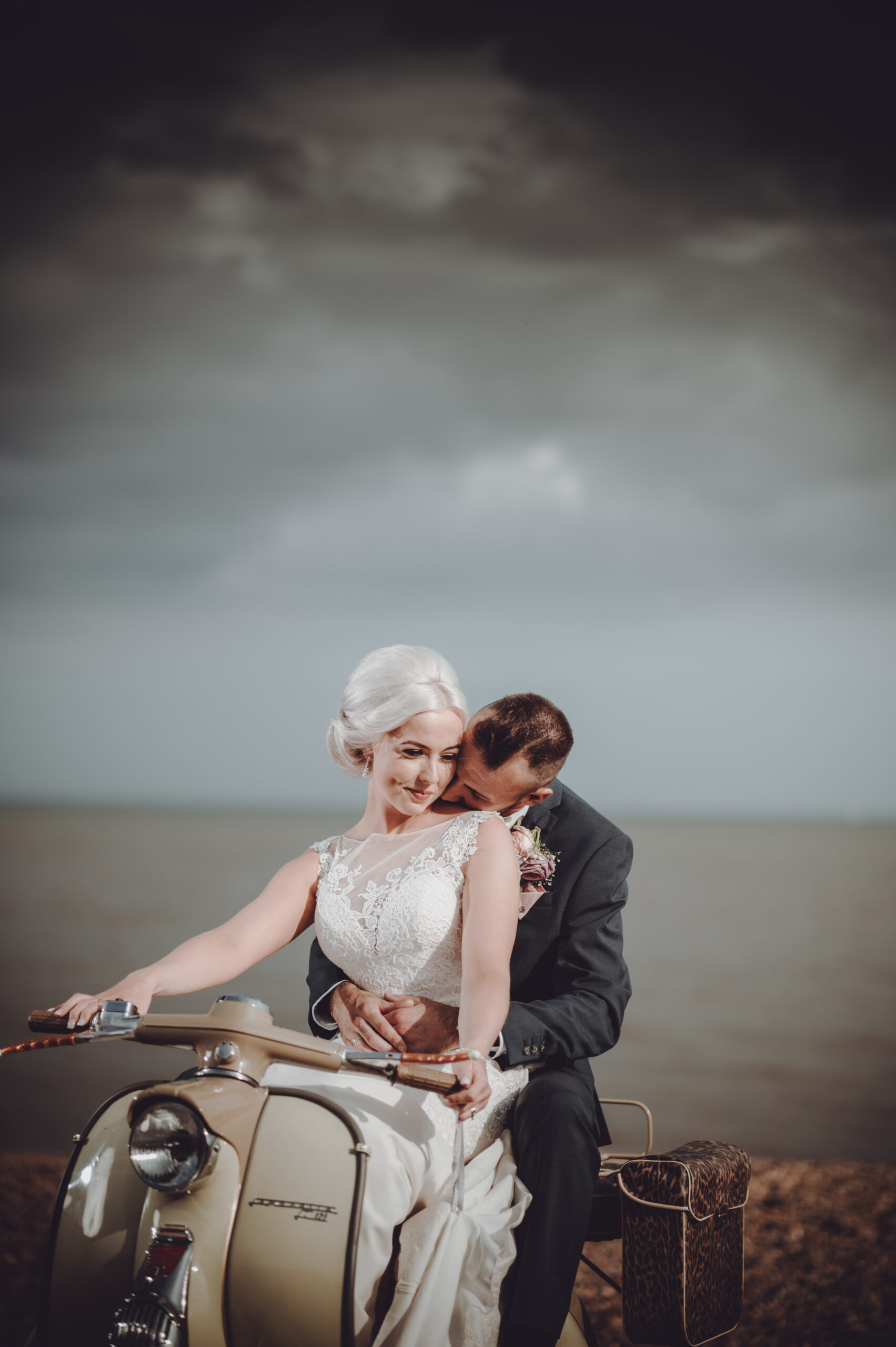 A bride and groom sitting on a vespa on the beach. (listing)