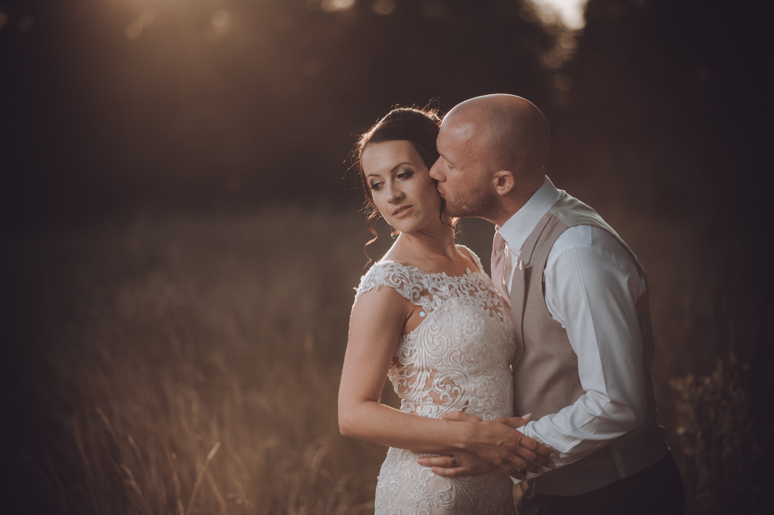 A bride and groom kissing in a field at sunset. (listing)