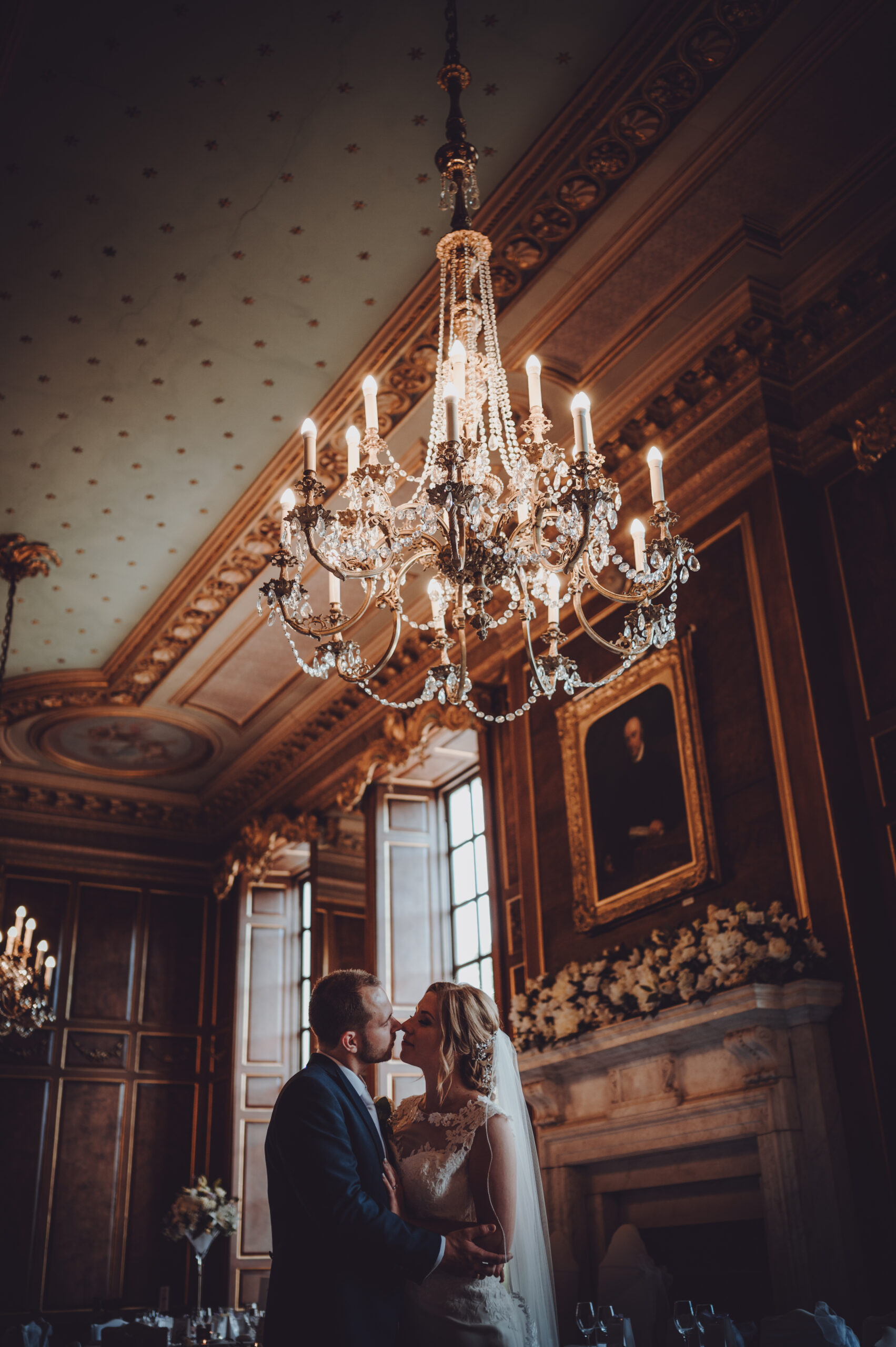 A bride and groom kiss in front of a chandelier. (listing)