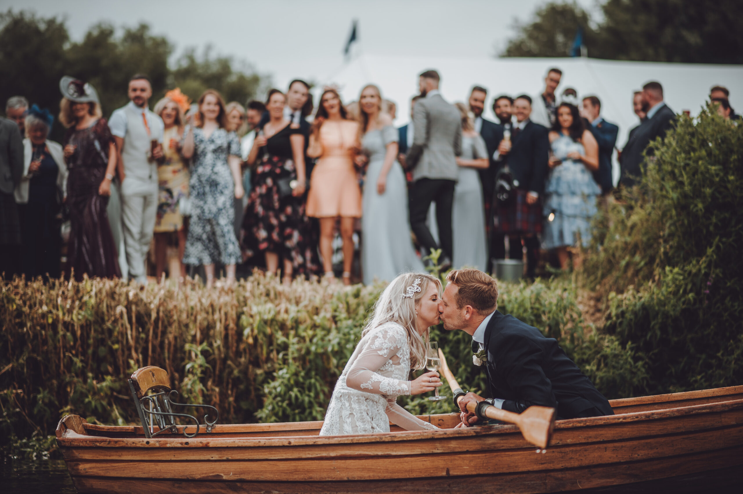 A bride and groom kissing in a boat in front of a crowd. (listing)