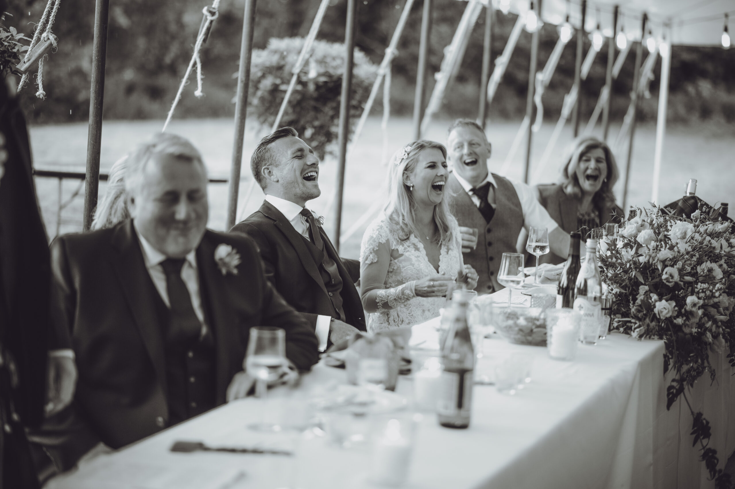 A black and white photo of a group of people laughing at a table. (listing)