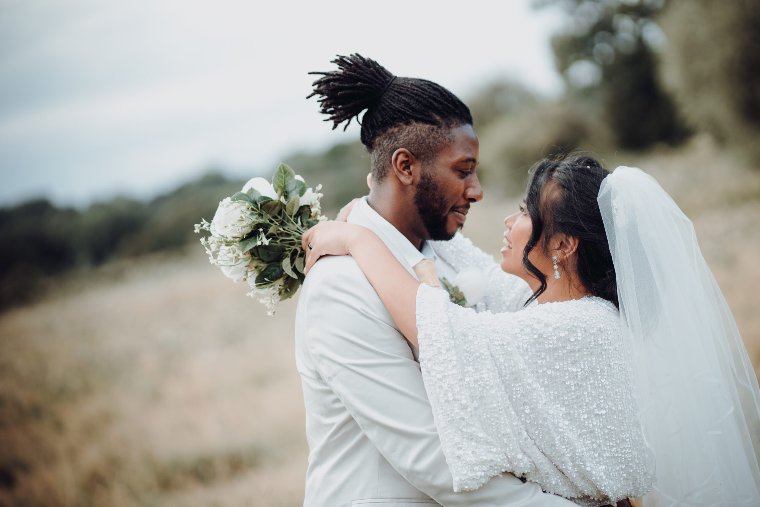 A bride and groom hugging in a field. (listing)