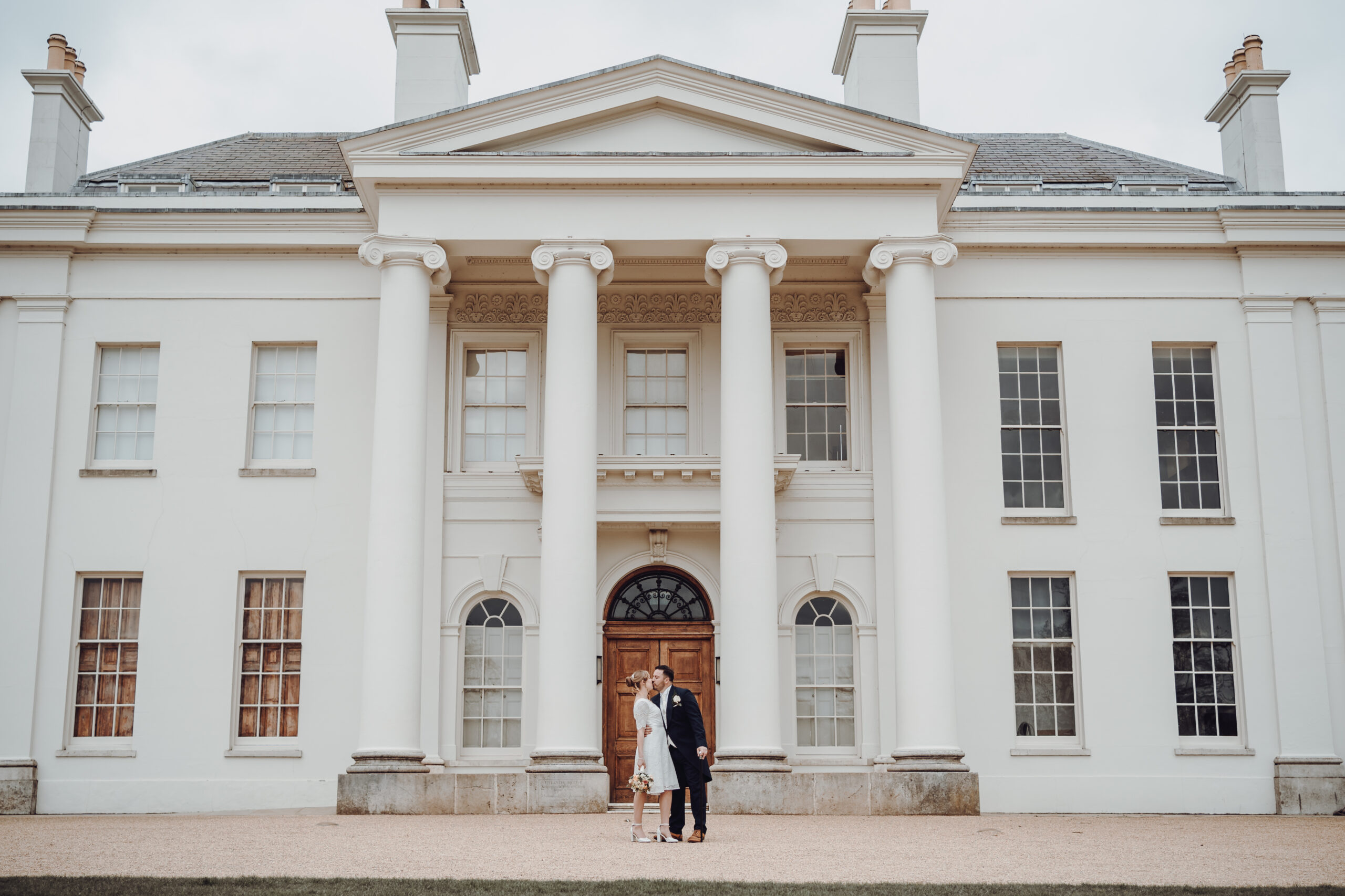 A bride and groom standing in front of a white mansion. (listing)