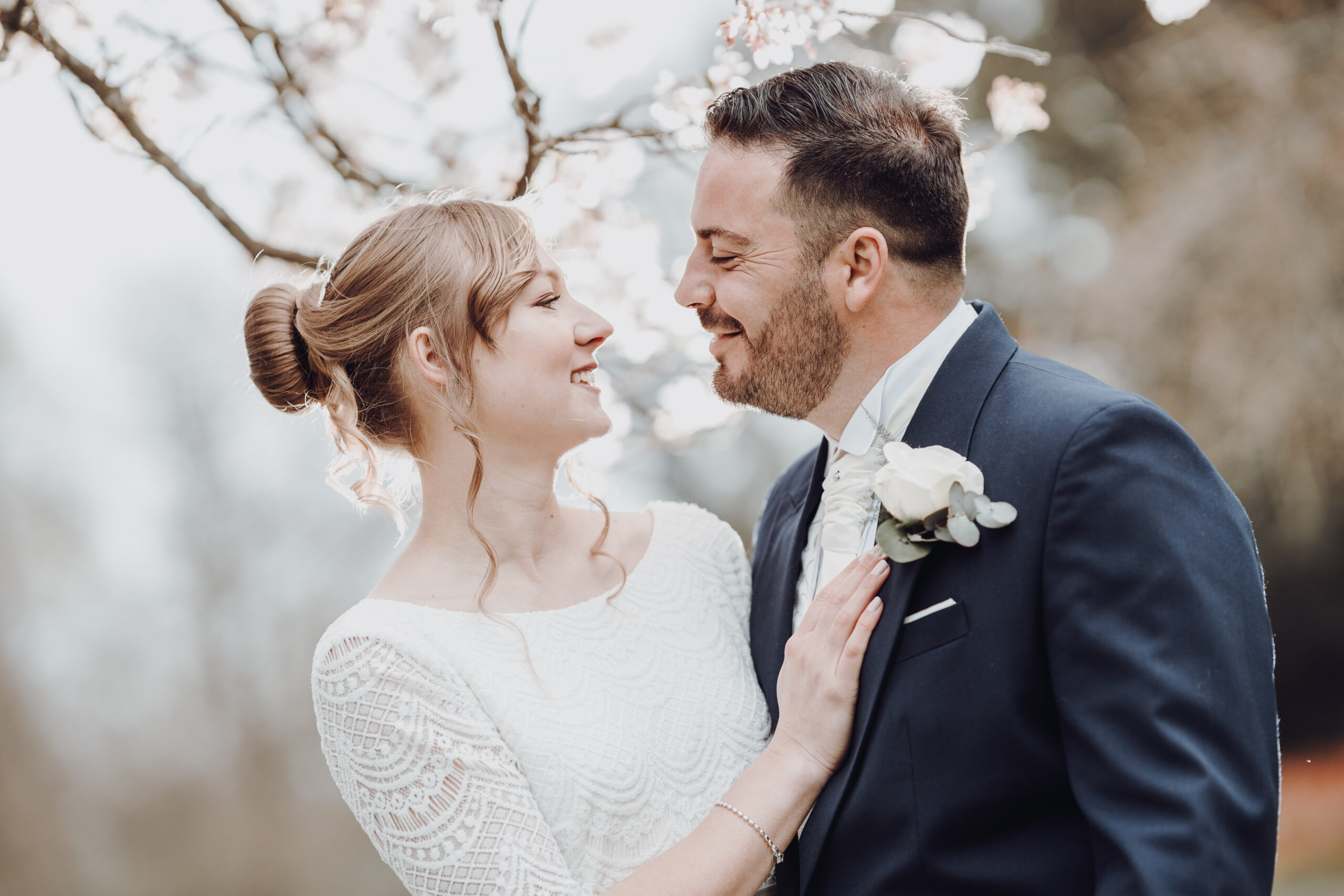 A bride and groom smiling under a cherry blossom tree. (listing)