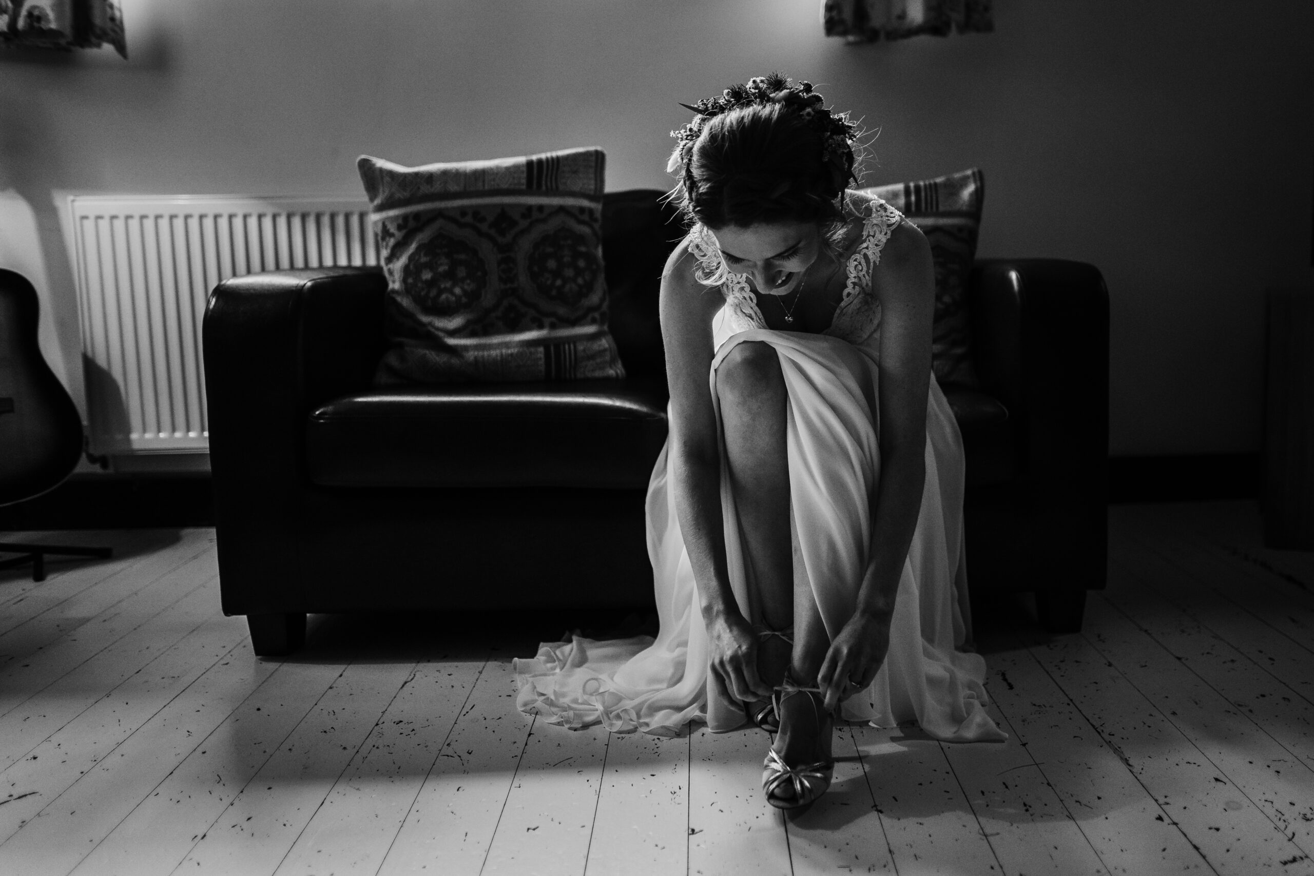 Black and white photo of a bride putting her shoes on. (listing)
