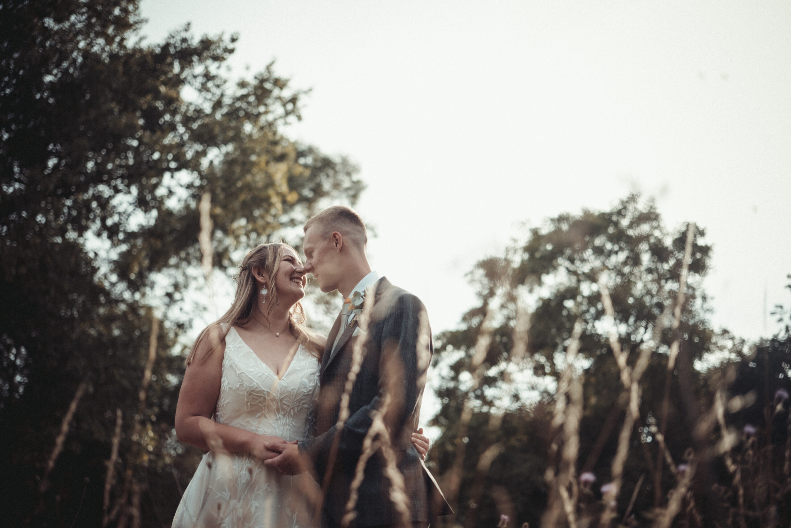 A bride and groom kissing in tall grass. (listing)