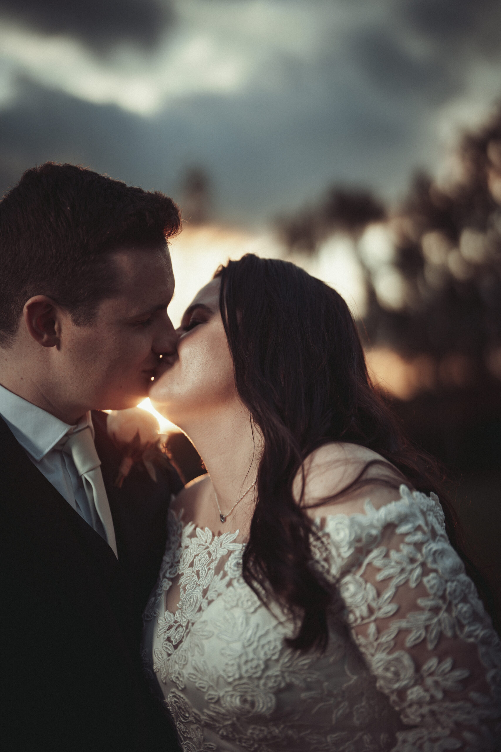 A bride and groom kissing in front of a sunset. (listing)