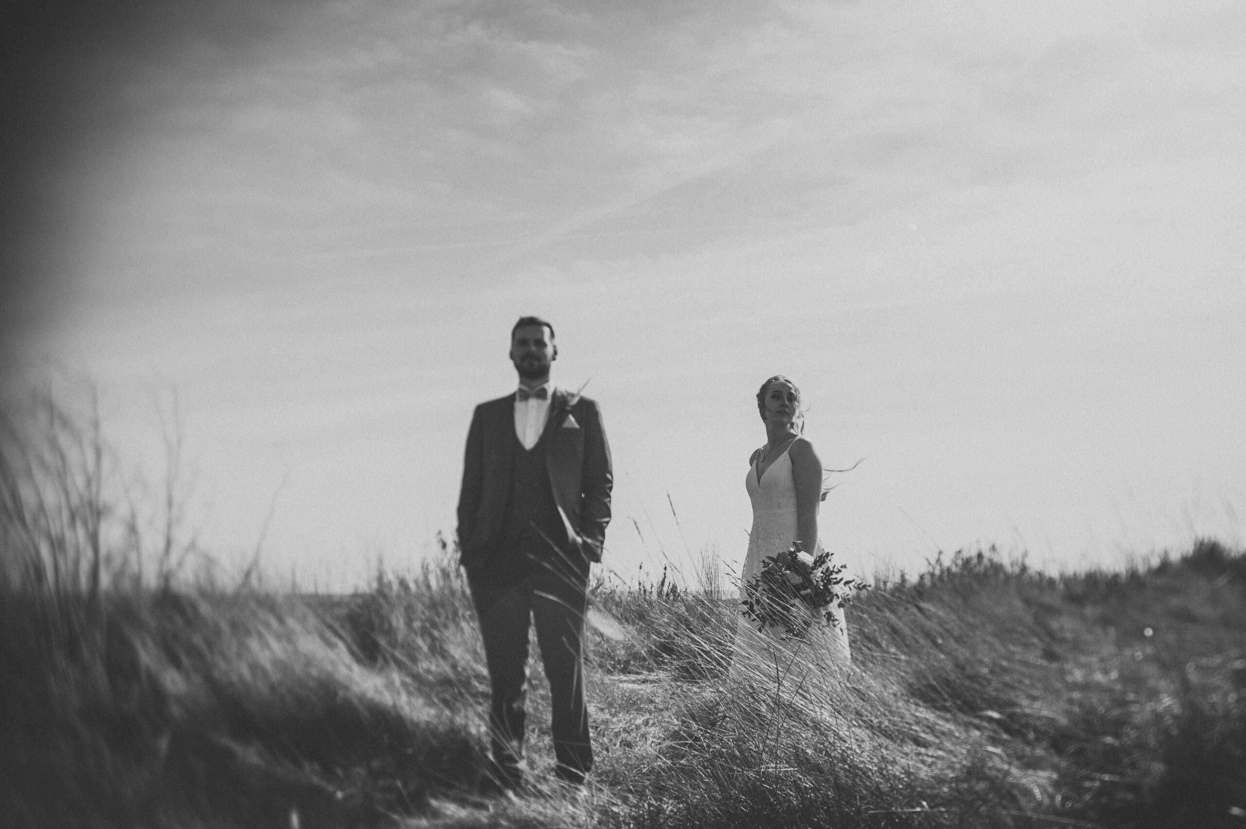 A bride and groom standing in a field of tall grass. (listing)
