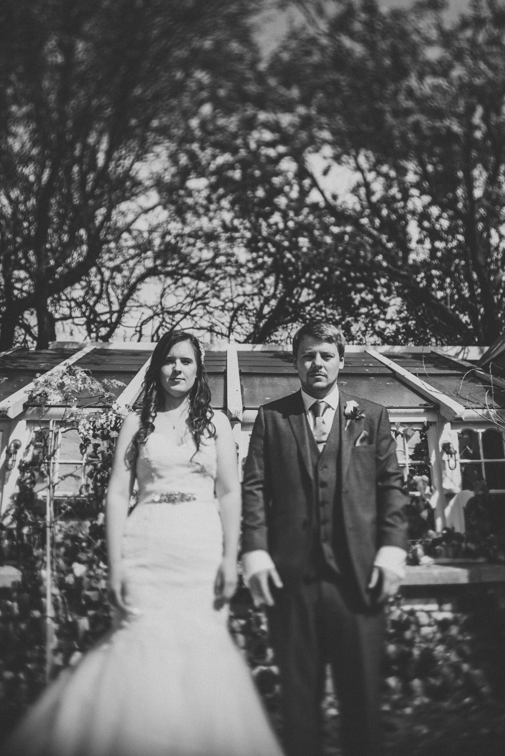 A bride and groom standing in front of a greenhouse. (listing)