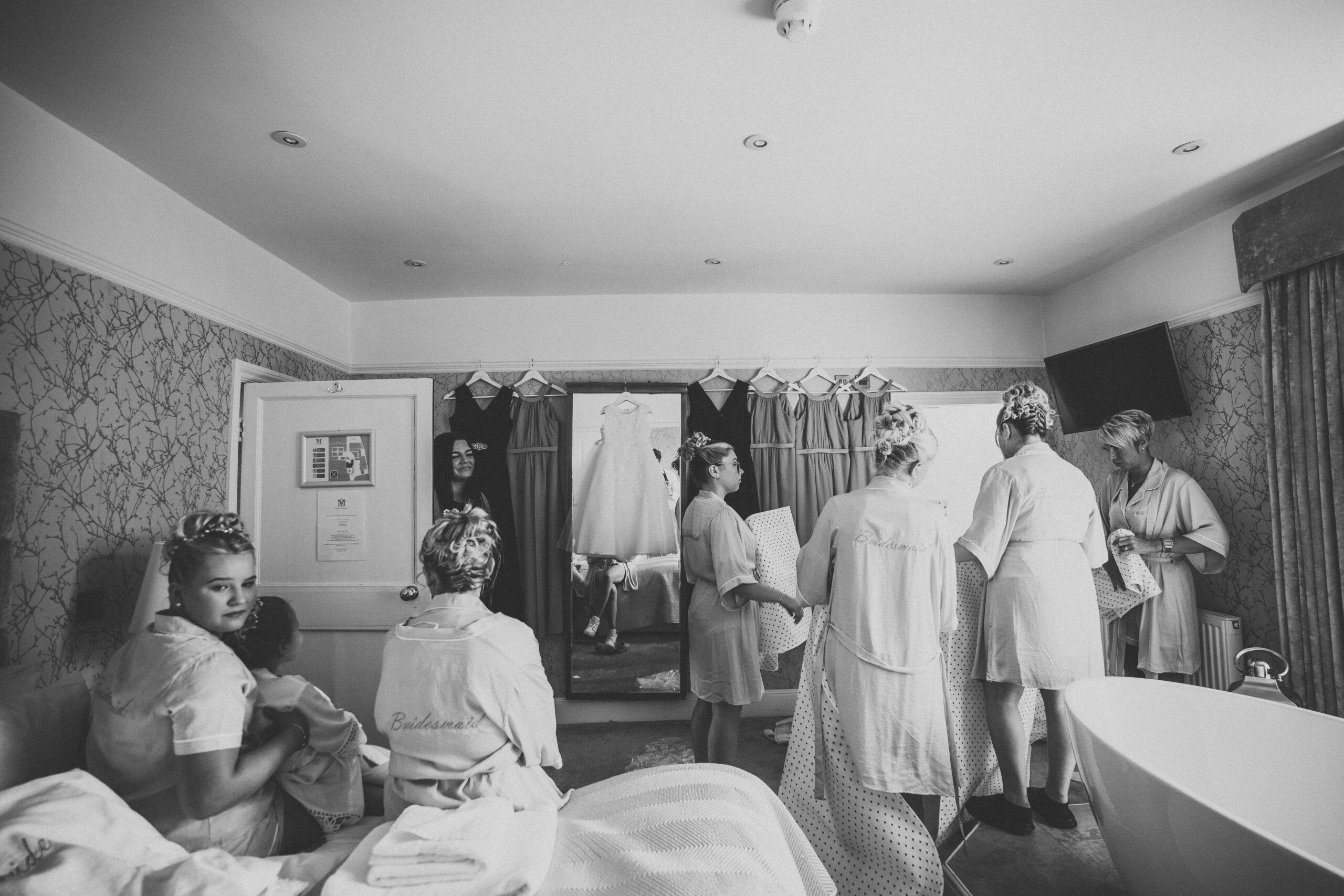 A black and white photo of bridesmaids getting ready in a hotel room. (listing)