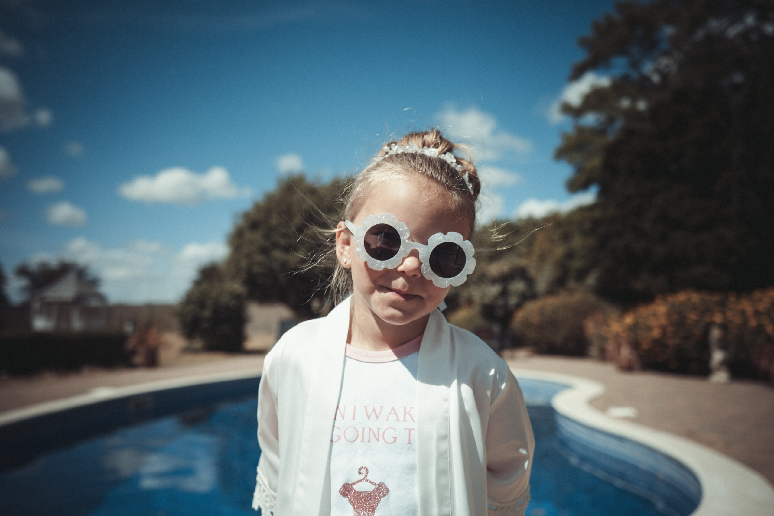 A little girl wearing sunglasses in front of a pool. (listing)