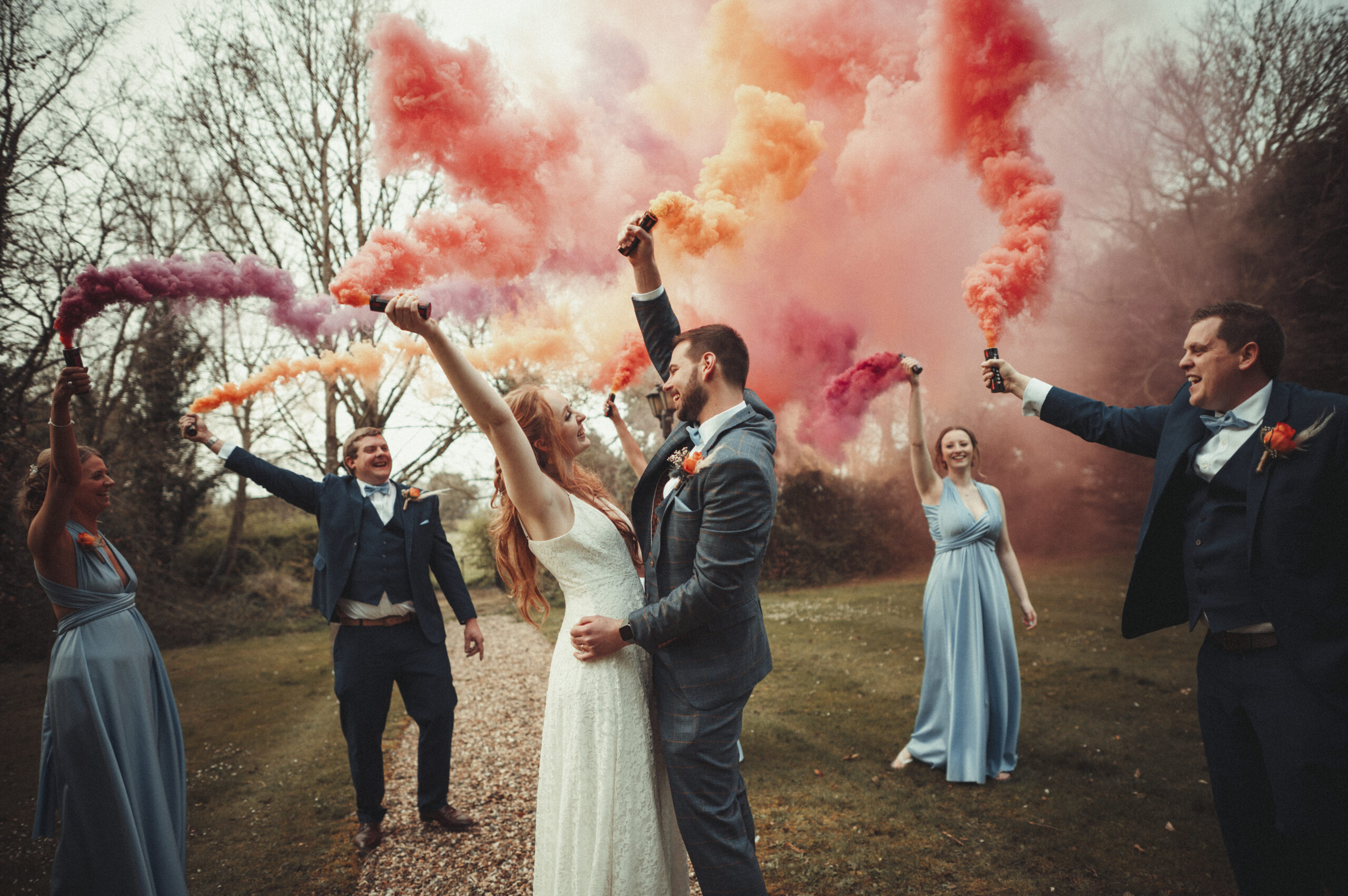 A group of bridesmaids and grooms holding colored smoke bombs. (listing)