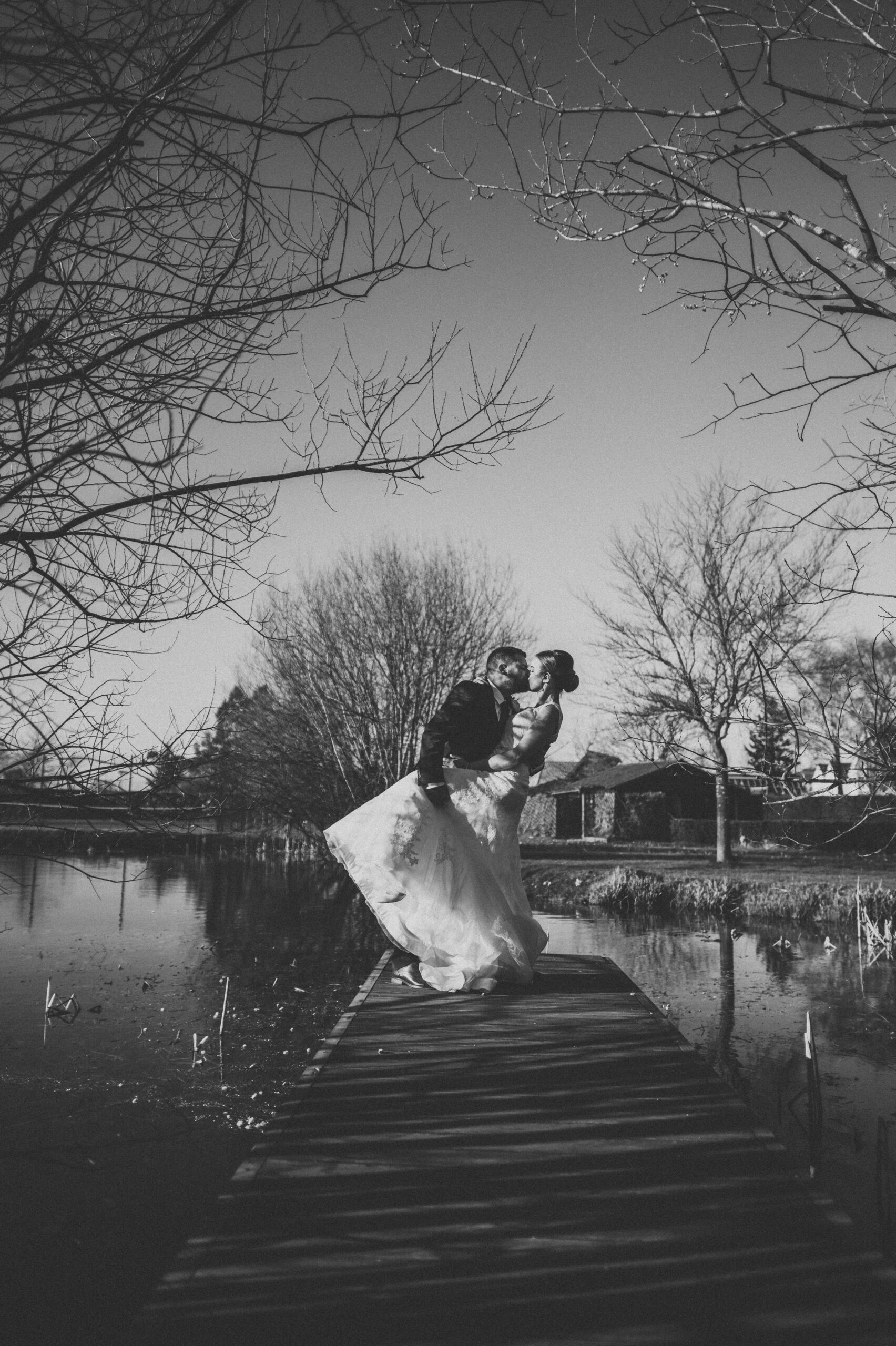 A bride and groom kissing on a dock in black and white. (listing)
