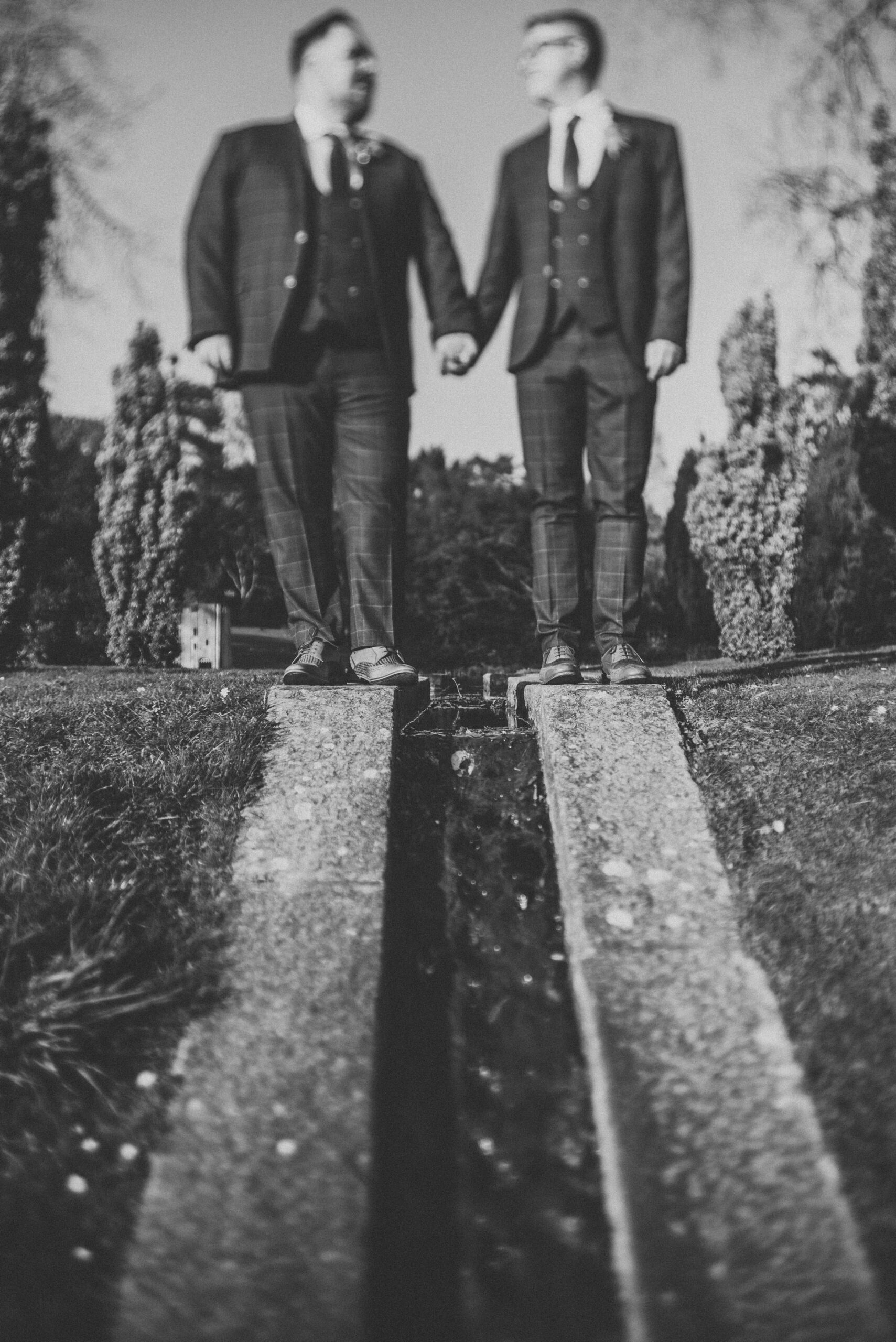 A black and white photo of two men holding hands in front of a waterfall. (listing)