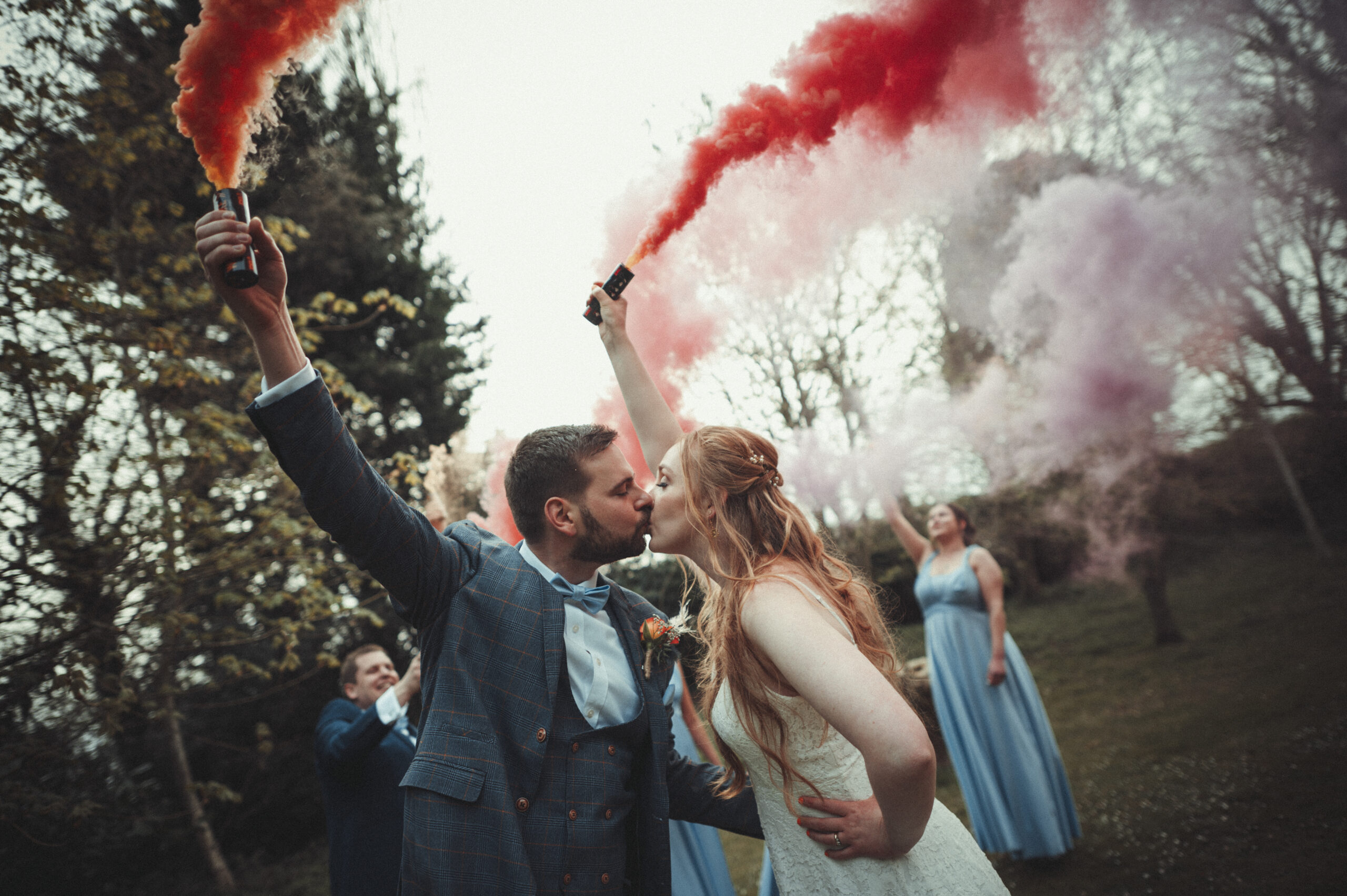 A bride and groom kissing with red and blue smoke bombs. (listing)