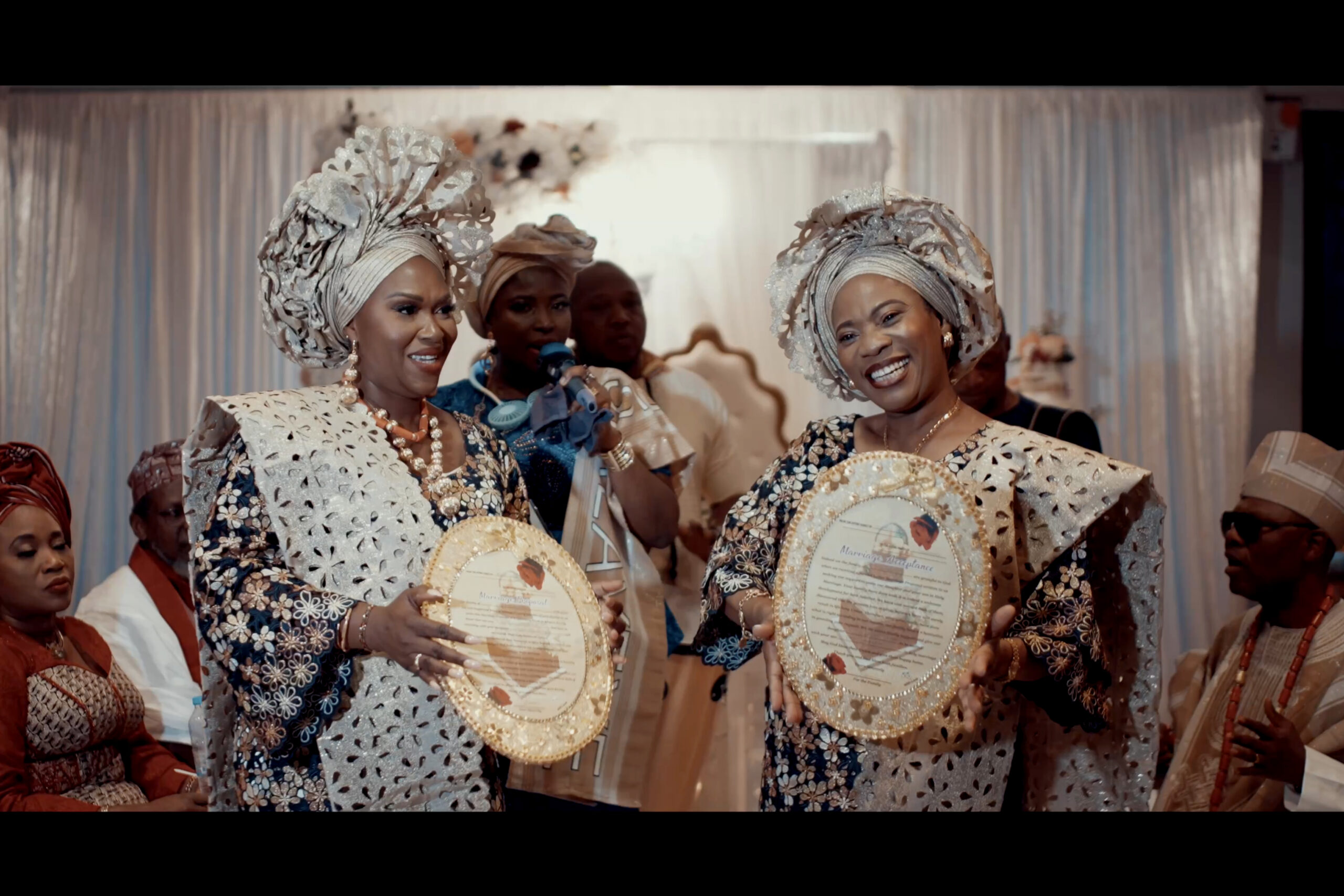 Two women in traditional attire are holding plates in front of each other. (listing)