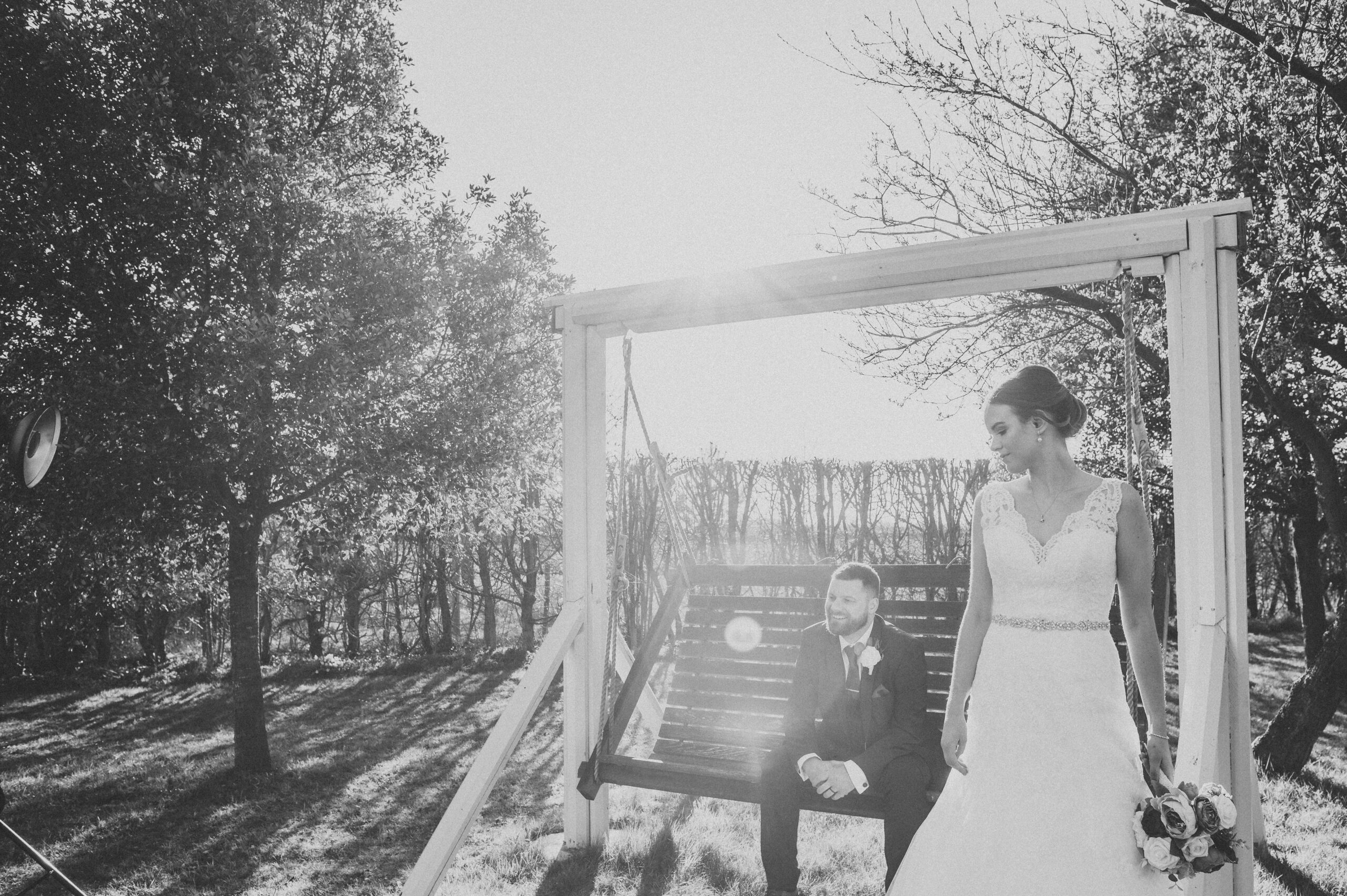 A black and white photo of a bride and groom on a swing. (listing)
