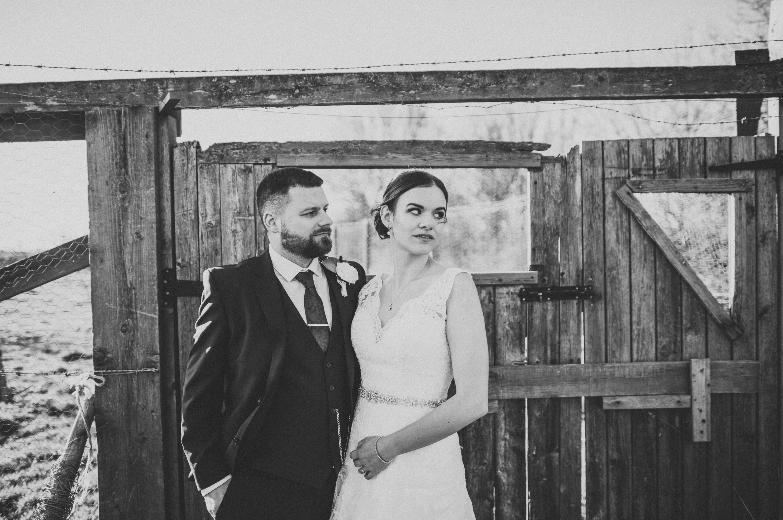 A bride and groom standing in front of a wooden gate. (listing)