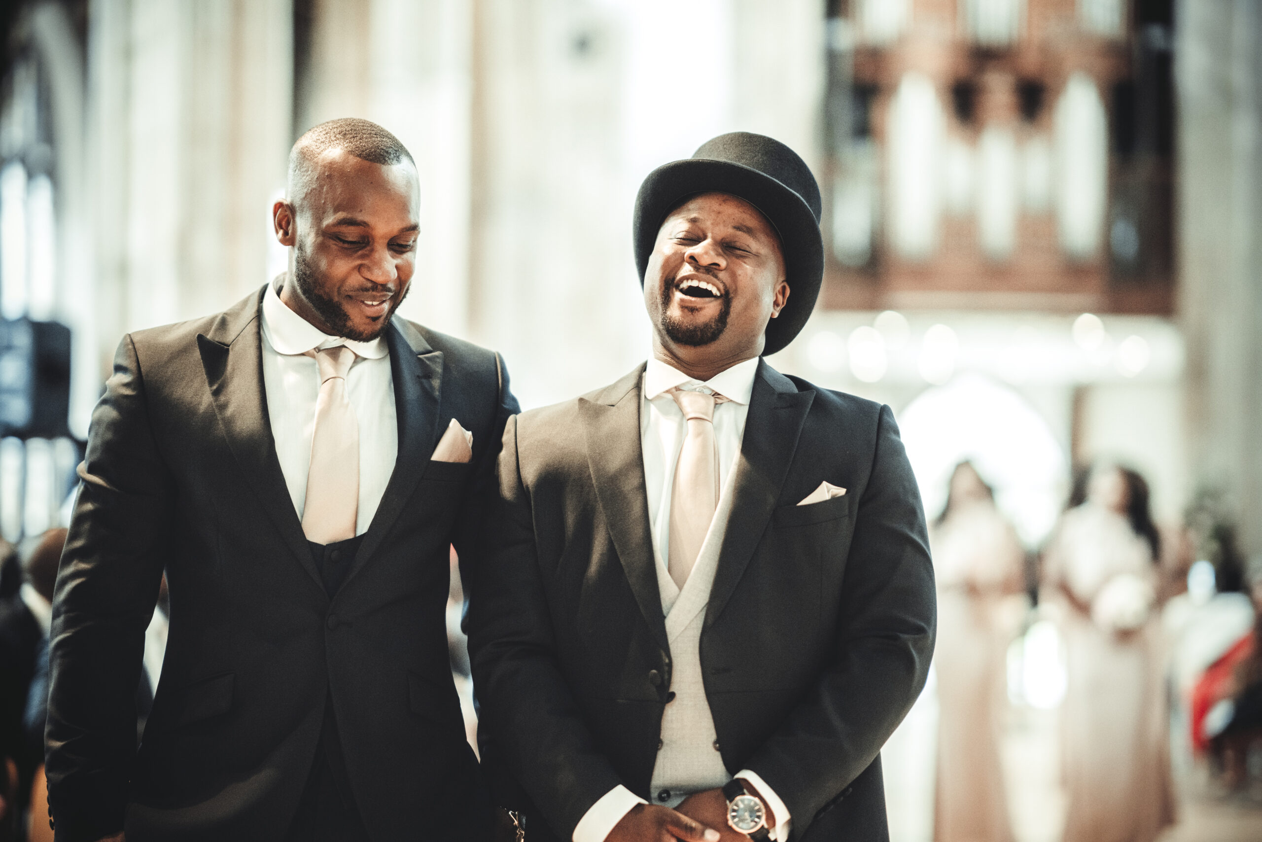 Two men in tuxedos laughing in a church. (listing)