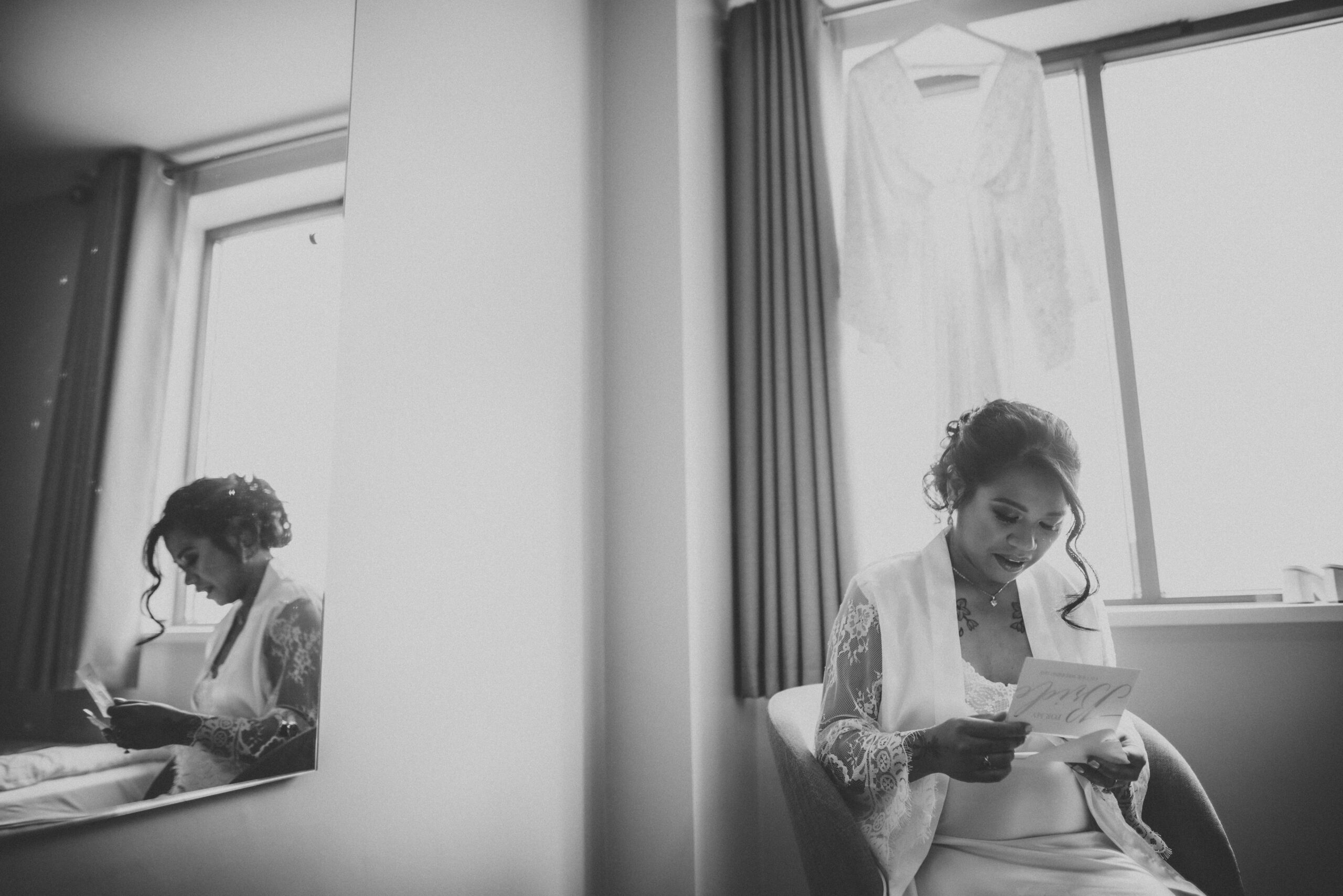 A bride is sitting in front of a mirror reading her wedding vows. (listing)