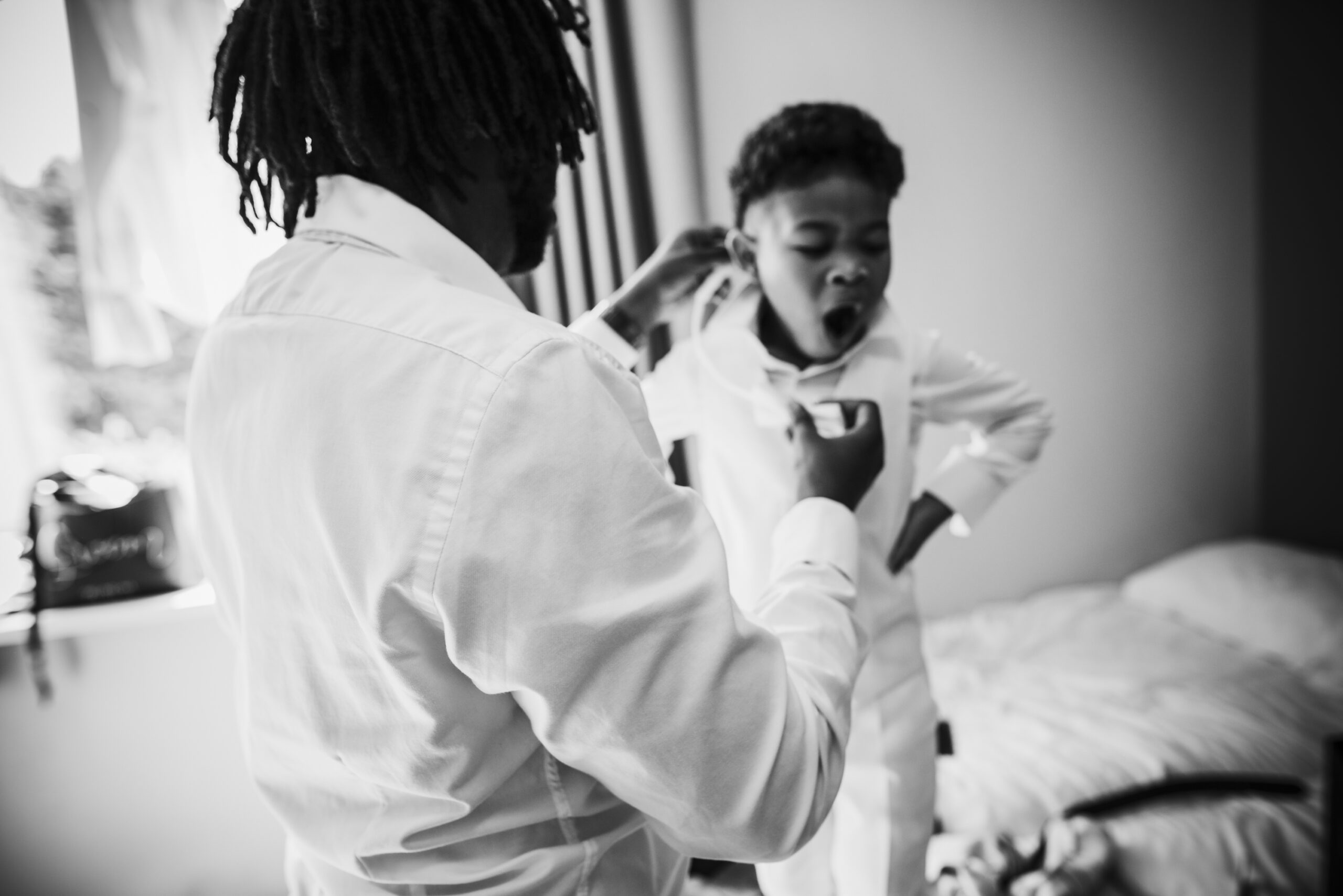 A black and white photo of a man putting on a tuxedo. (listing)
