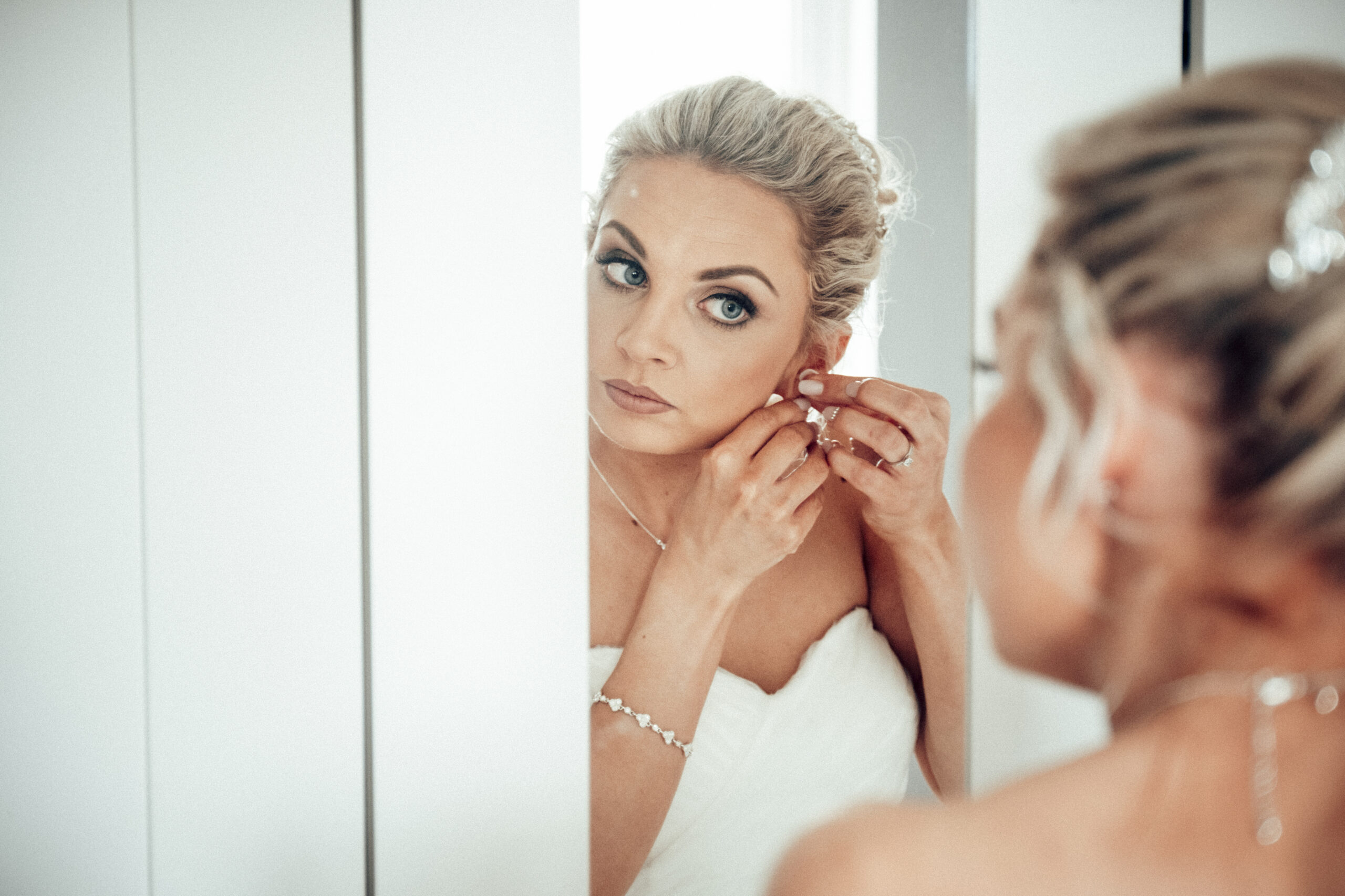 A bride putting on her wedding earring in front of a mirror. (listing)