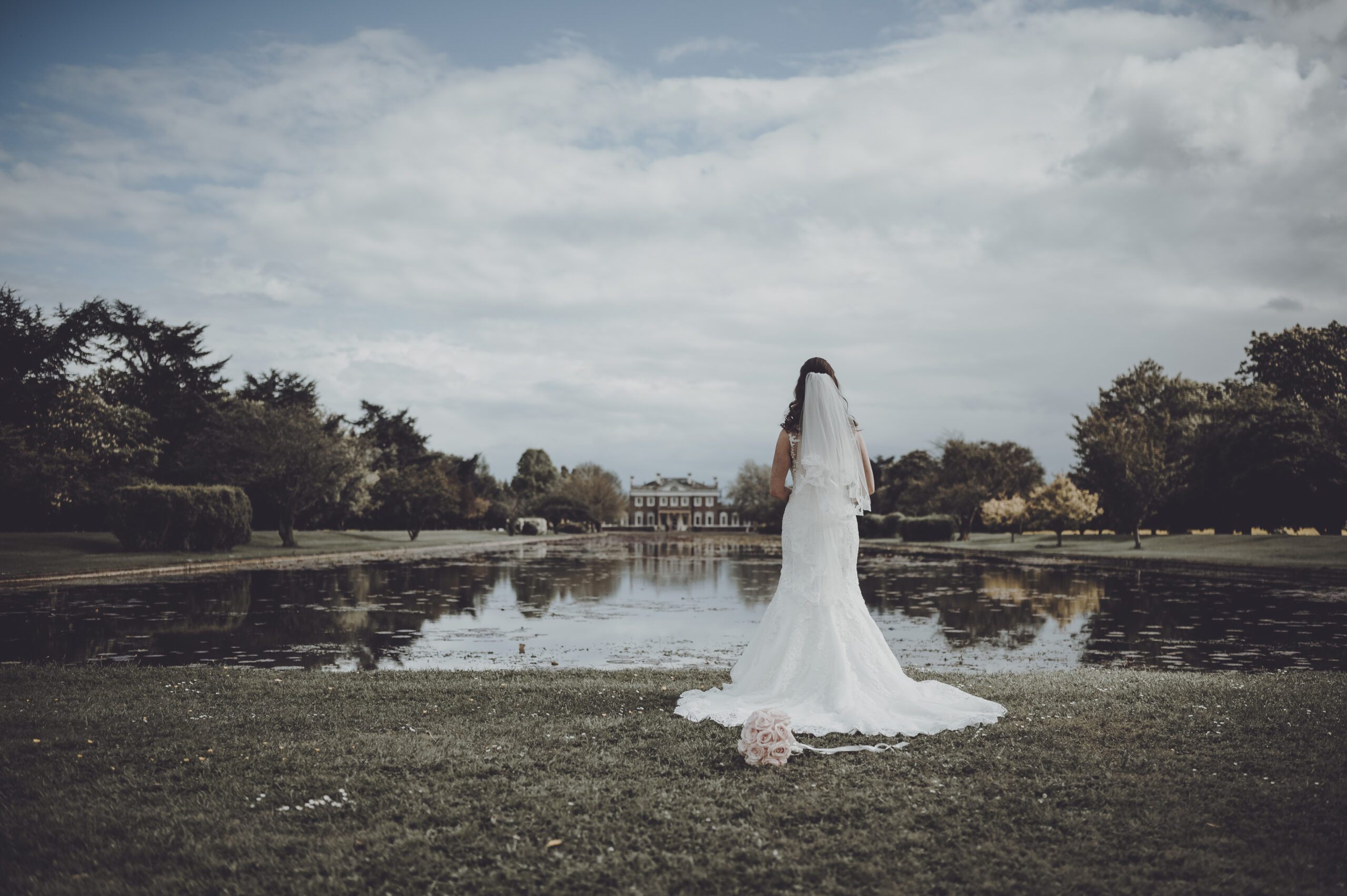 A bride is standing in front of a pond. (listing)