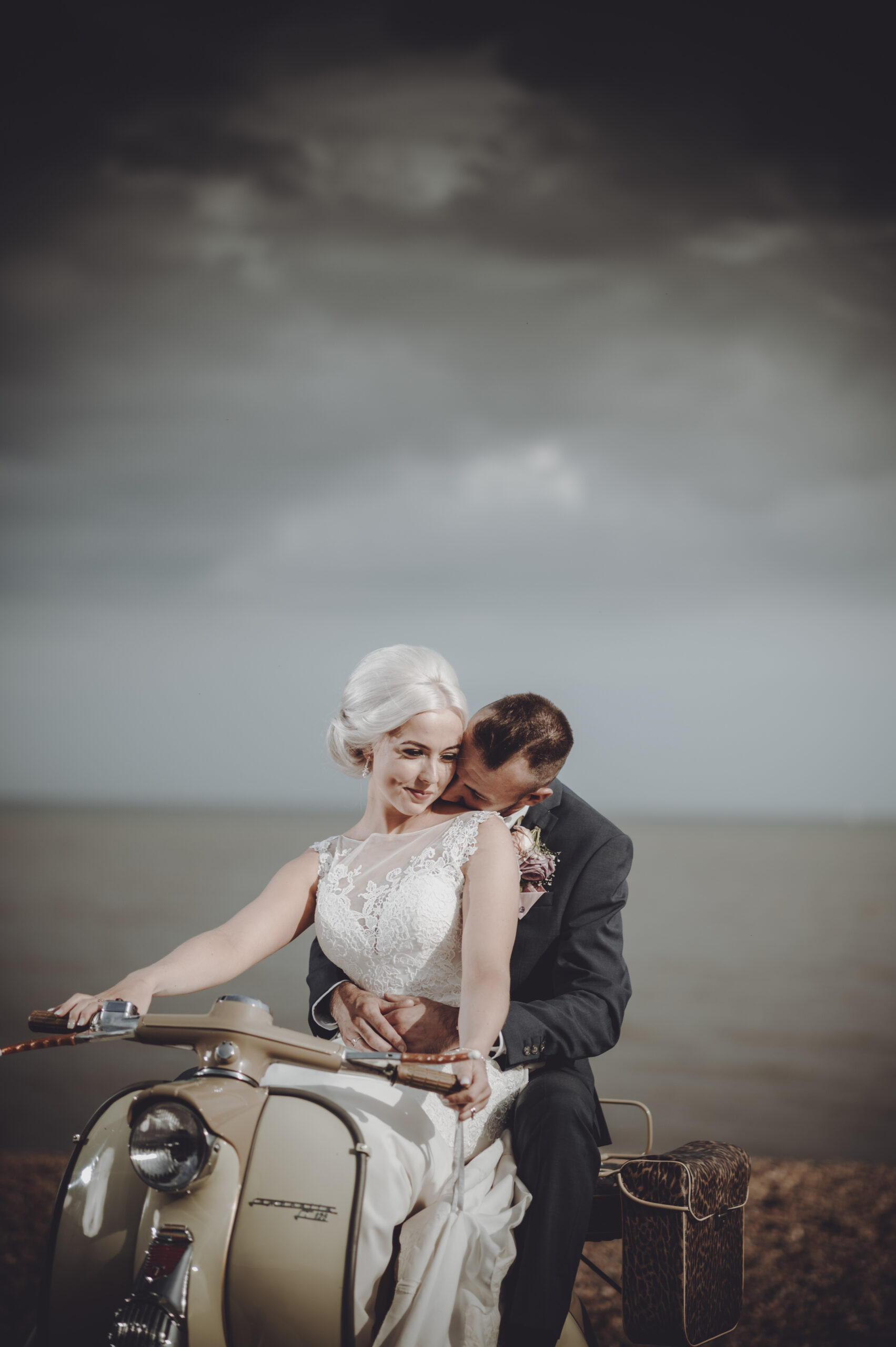 A bride and groom sitting on a vespa on the beach. (listing)