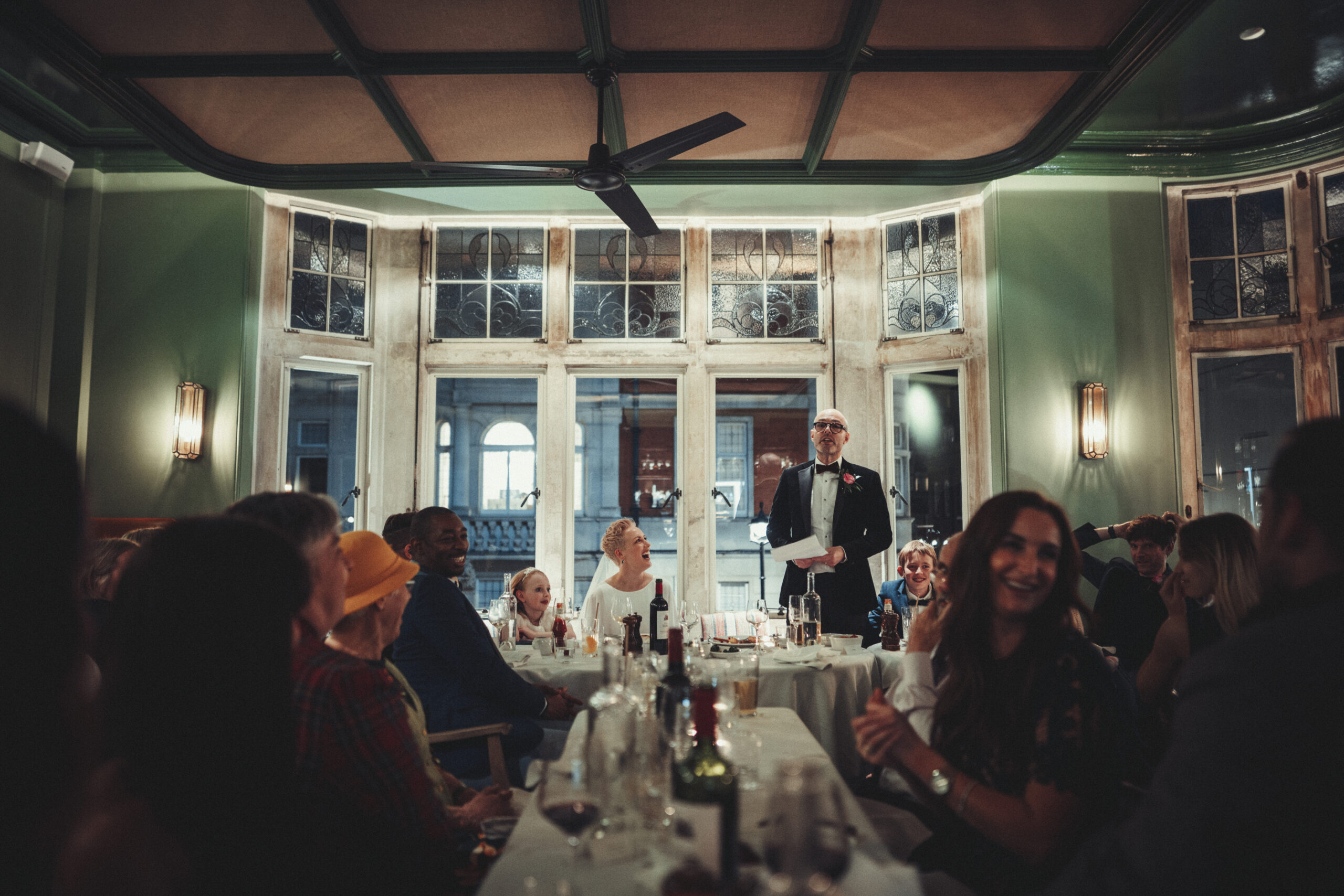 A man speaking to a group of people in a restaurant. (listing)