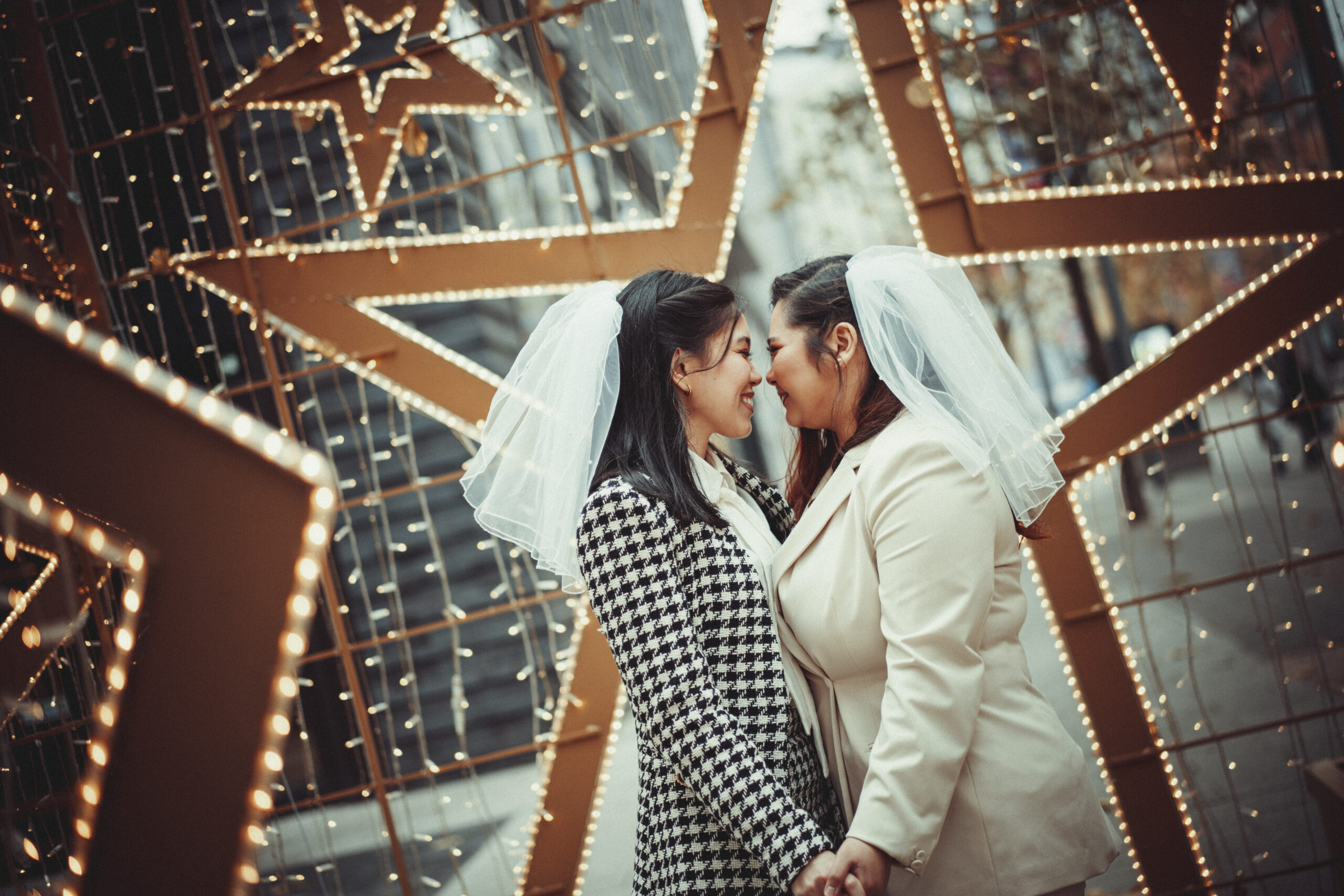 Two brides hugging in front of star lights. (listing)
