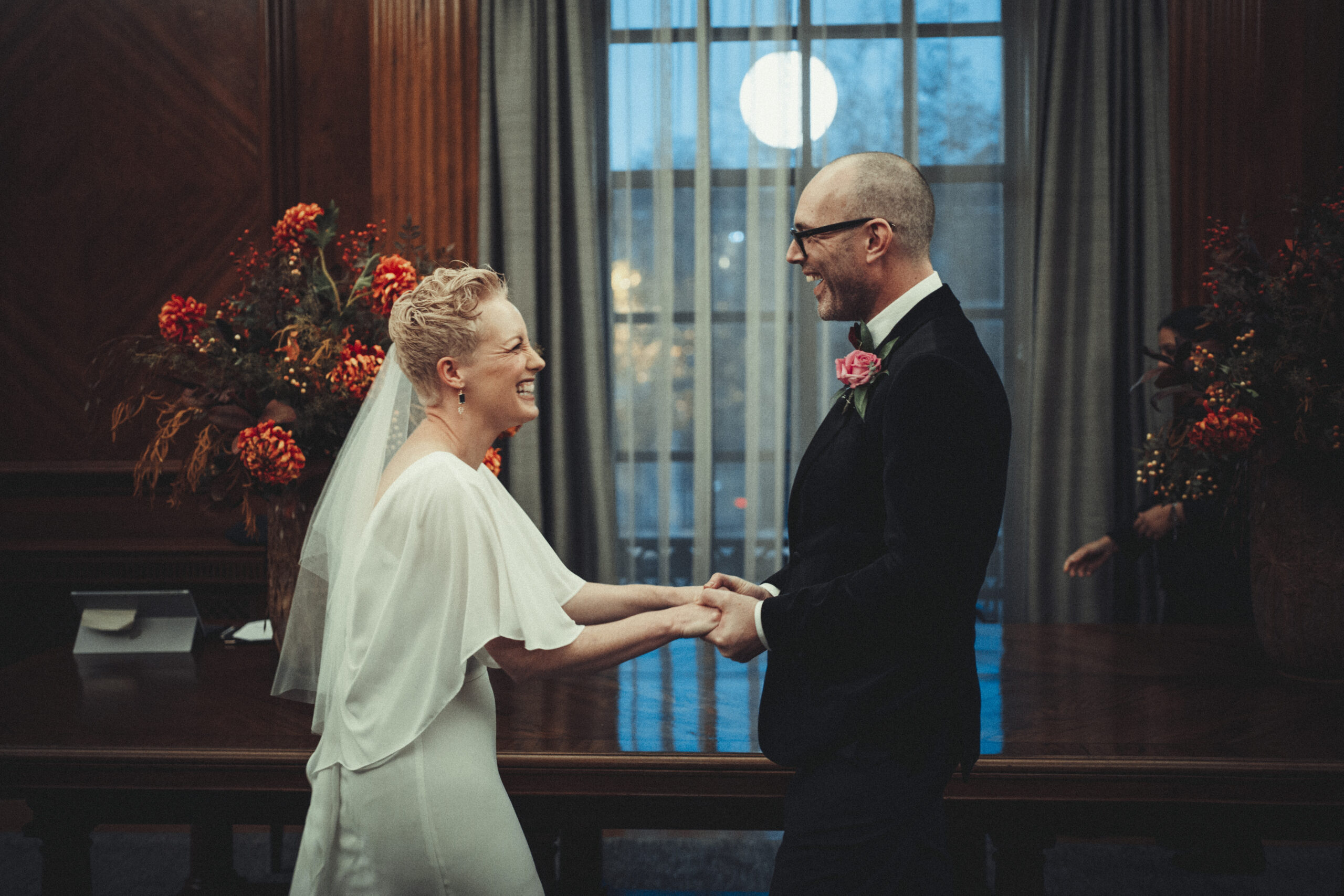 A bride and groom standing in front of a large window. (listing)